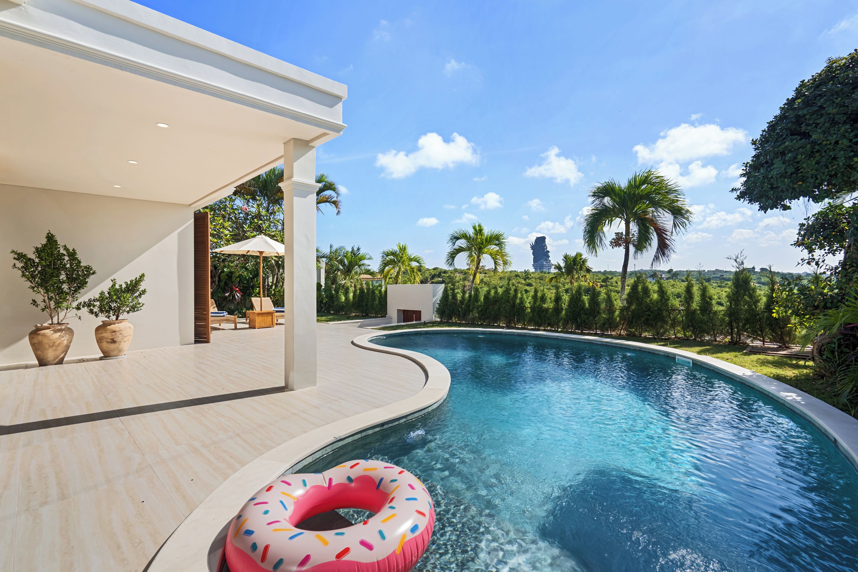 A swimming pool with a curved edge, surrounded by a patio area with lounge chairs and potted plants.