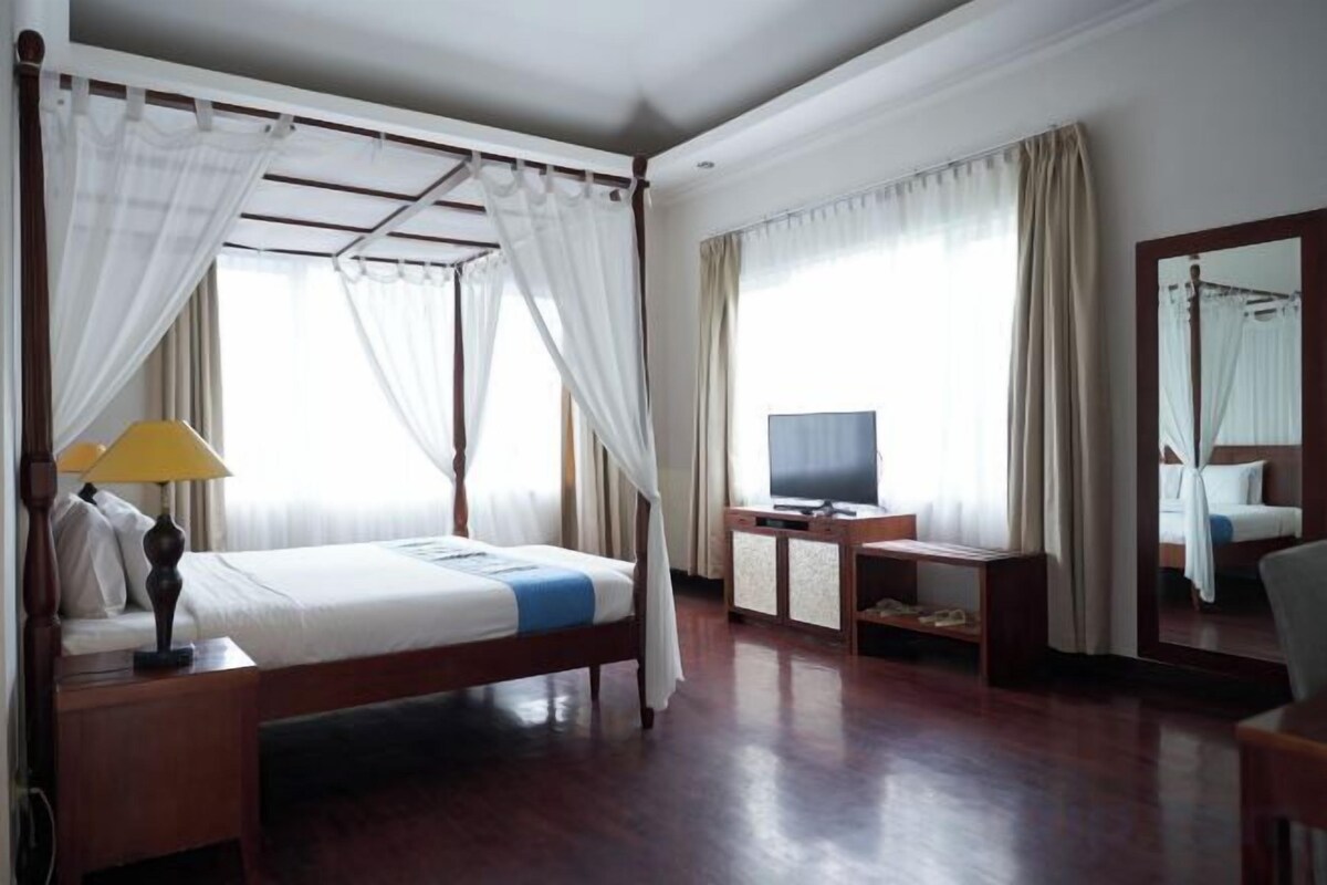 A four-poster bed with a canopy, a television on a side table, and a mirror on the wall.