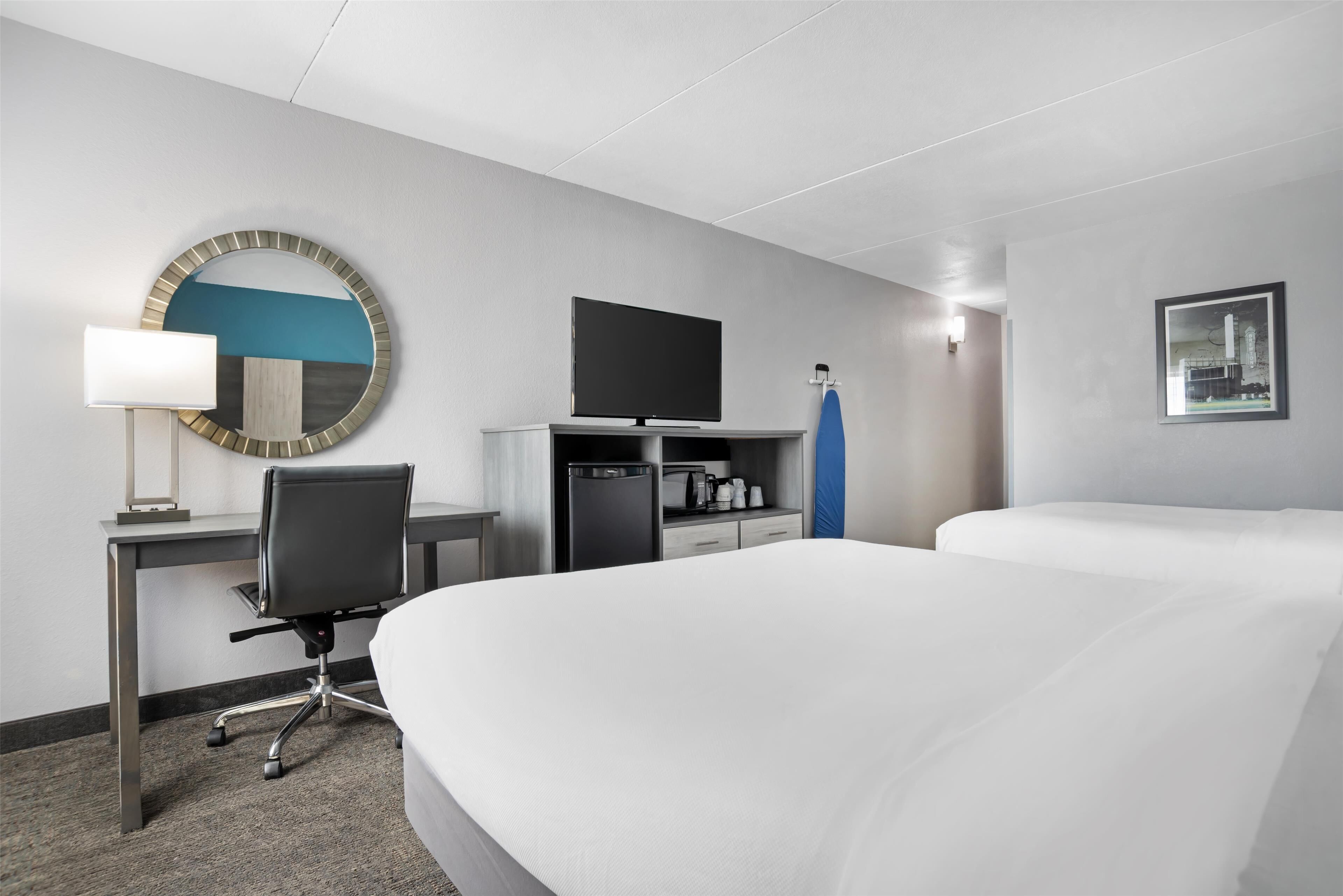 Una habitación de hotel con cama, escritorio, silla, televisión, cafetera y espejo.