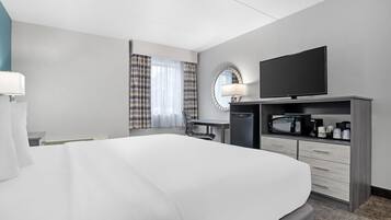 A hotel room with a large bed, a desk with a chair, a television, a microwave, and a coffee maker.