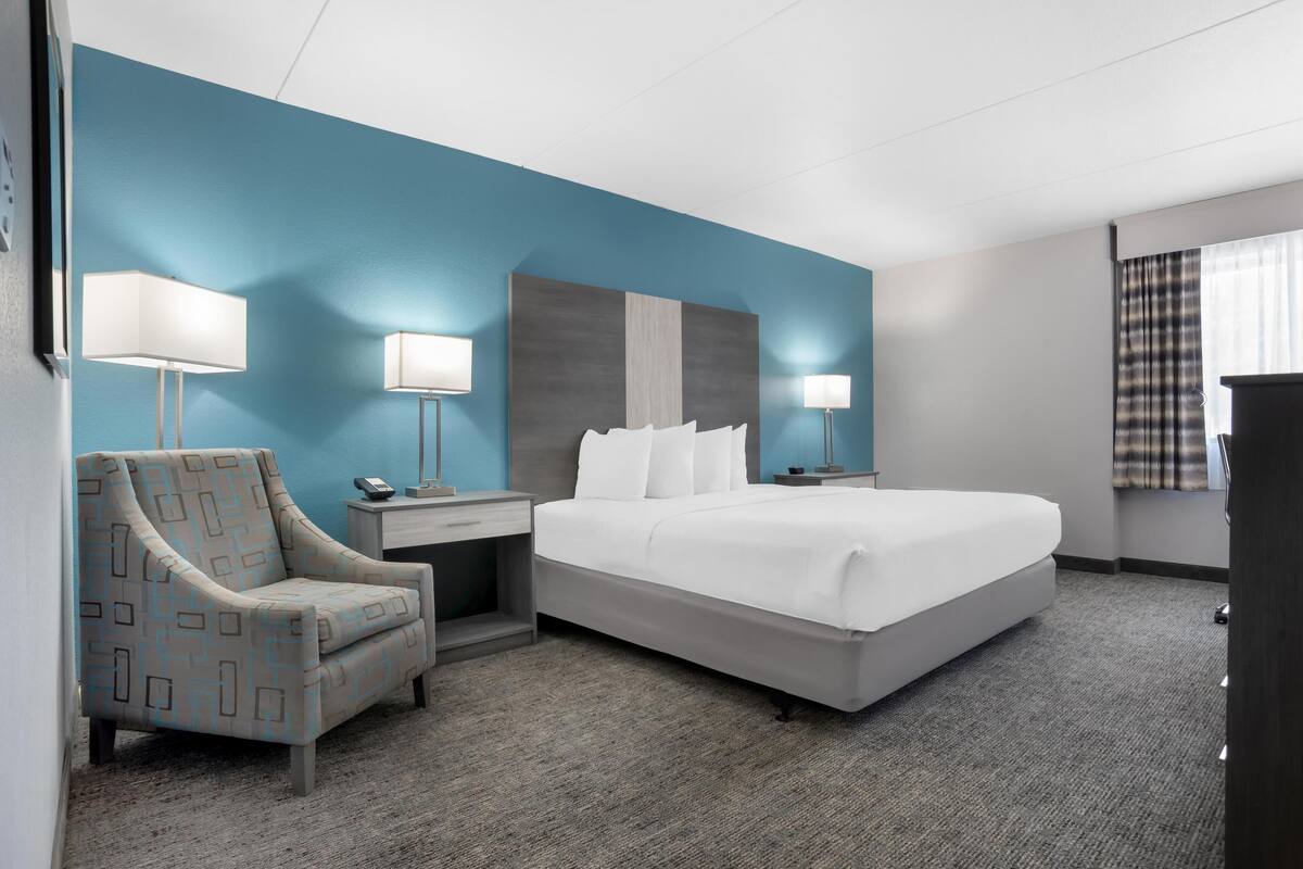 Ein Hotelzimmer mit einem großen Bett, zwei Nachttischen, einem Sessel und einem an der Wand befestigten Fernseher.