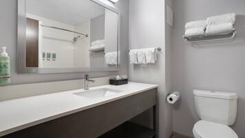 A modern bathroom with a white sink, a large mirror, a toilet, and a towel rack.
