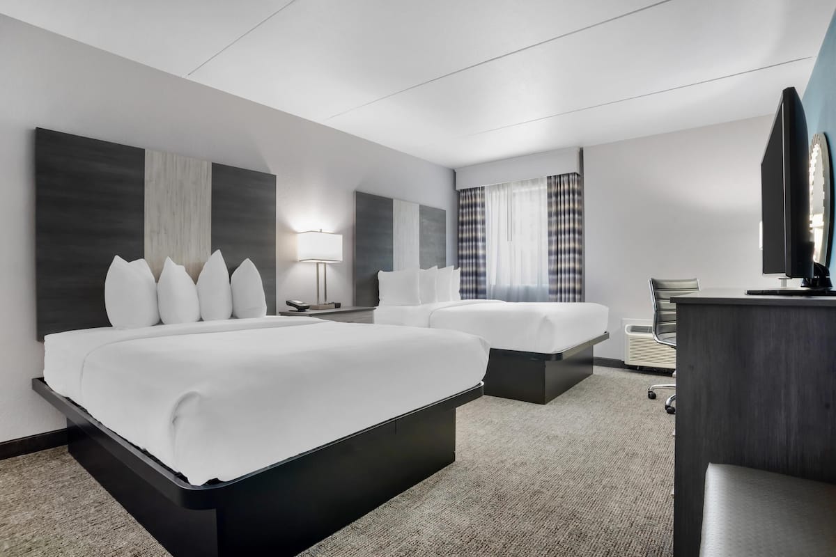 Ein Hotelzimmer mit zwei Betten, einem Schreibtisch, einem Stuhl, einer Lampe und einem großen Spiegel.