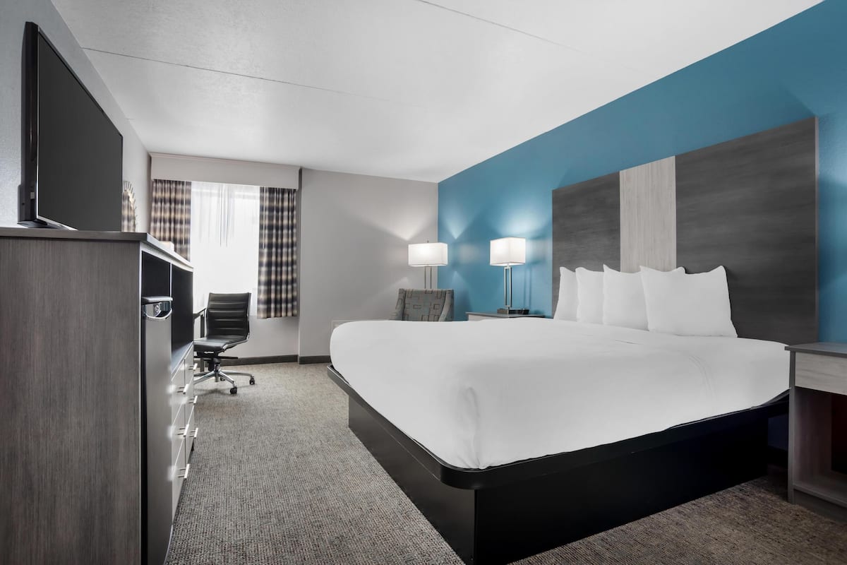 Ein Hotelzimmer mit einem großen Bett, einem Schreibtisch mit Stuhl, einem Fernseher und zwei Lampen.