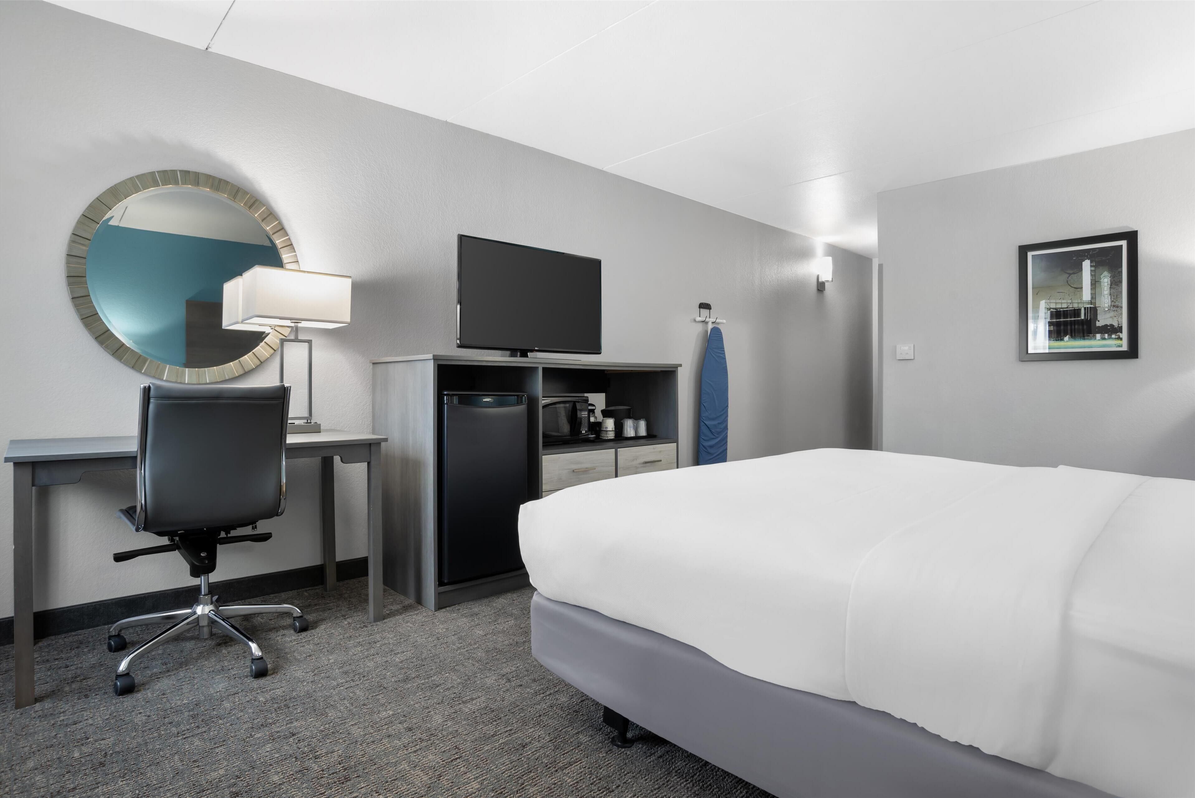 Habitación de hotel con cama, escritorio, silla, televisor y un espejo grande.