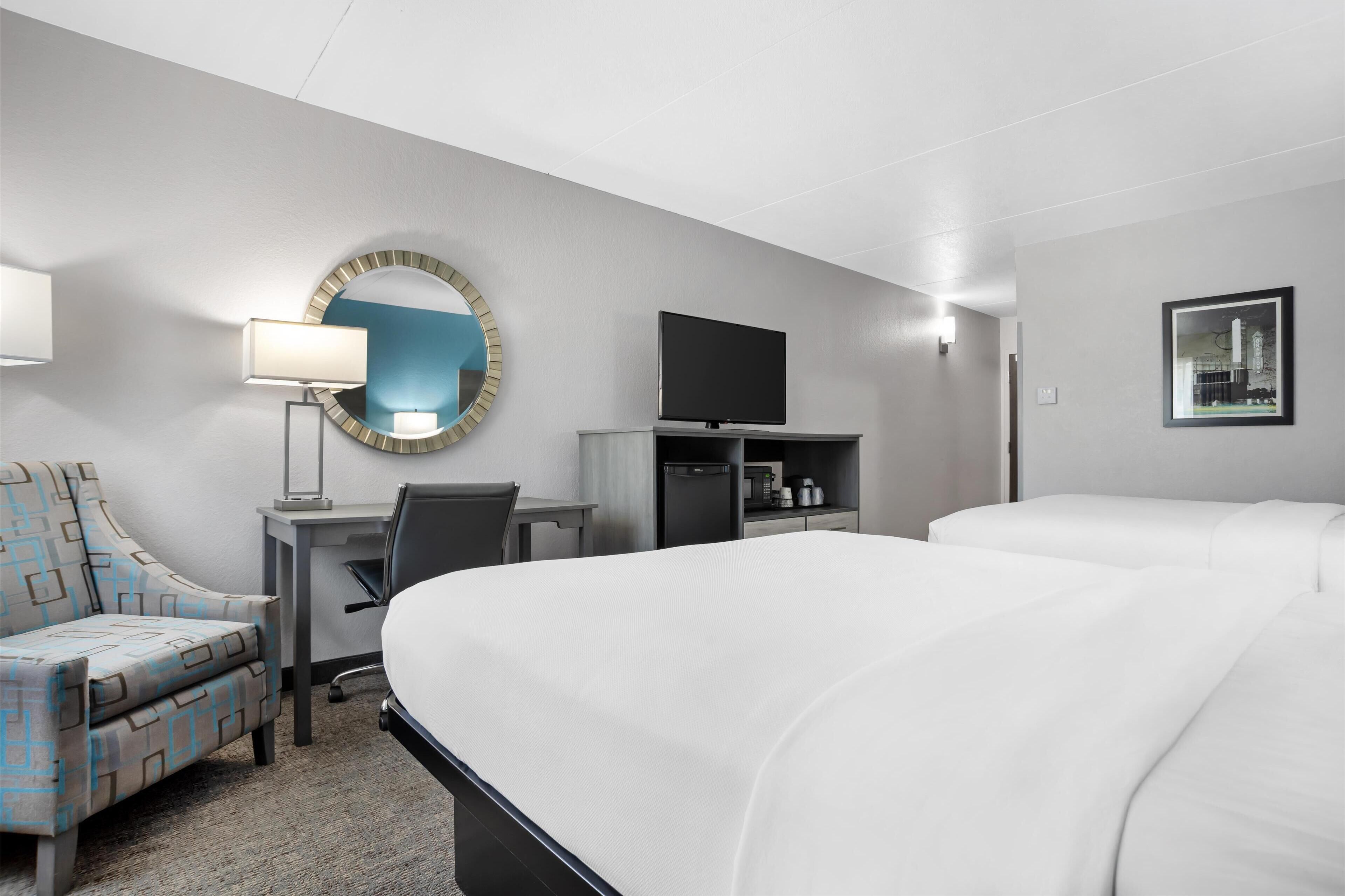 A hotel room with a large bed, a desk with a chair, a television, a mirror, and a framed picture on the wall.