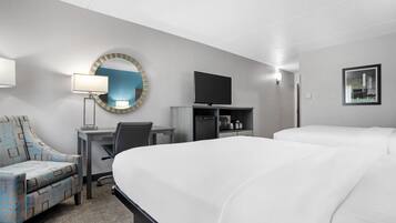 A hotel room with a large bed, a desk with a chair, a television, a mirror, and a framed picture on the wall.