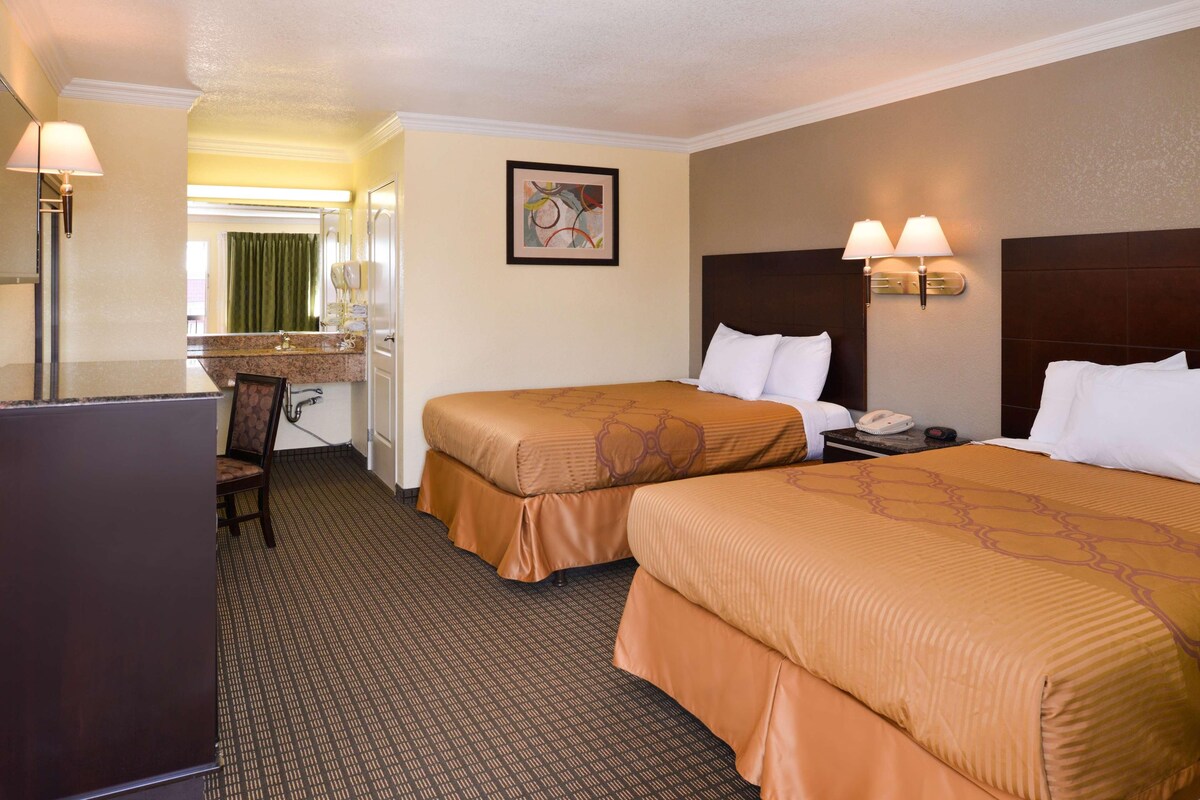 A hotel room with two beds, a desk, a chair, and a mirror.