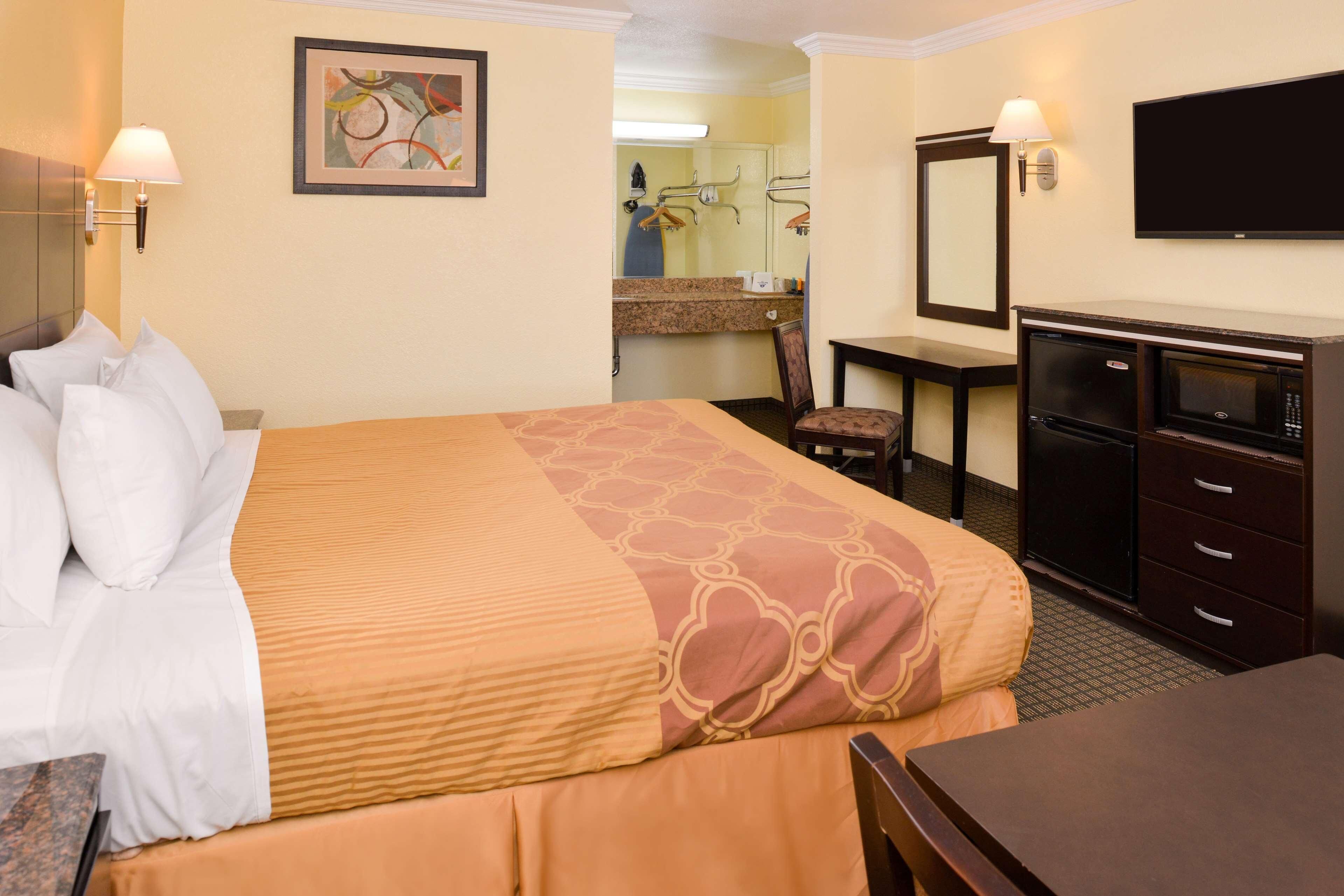 A hotel room with a bed, a desk, a chair, a television, a microwave, and a bathroom visible in the background.