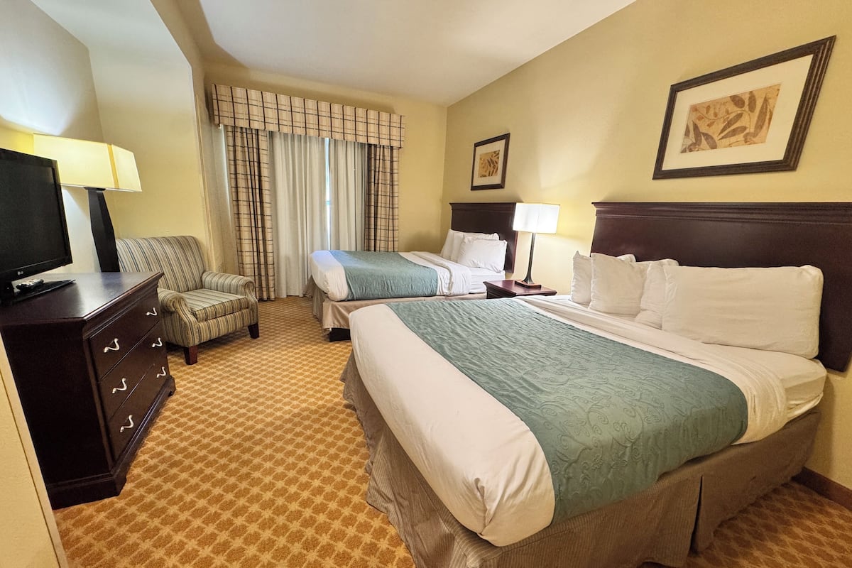 A hotel room with a large bed, a smaller bed, a TV, a desk, and a chair.