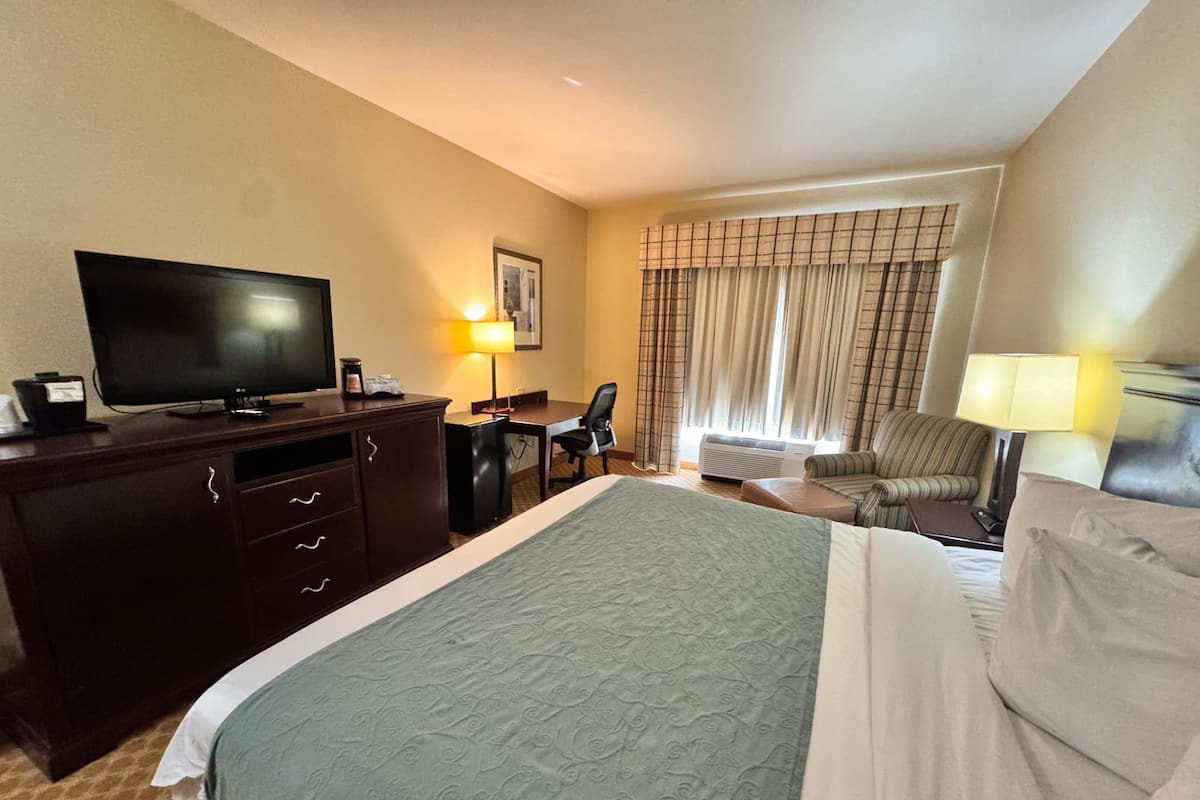 A hotel room with a large bed, a desk, a chair, a television, and a window with curtains.