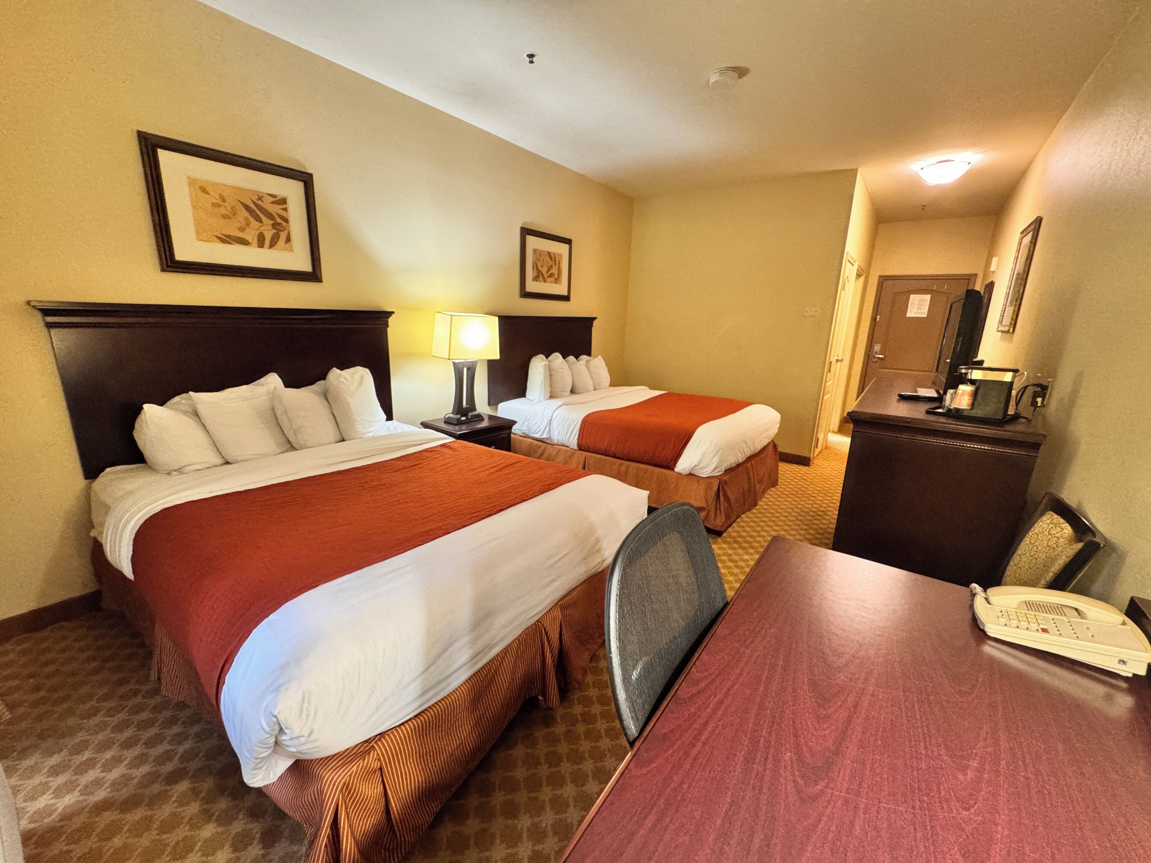 A hotel room with two beds, a desk, a chair, a telephone, and a desk lamp.