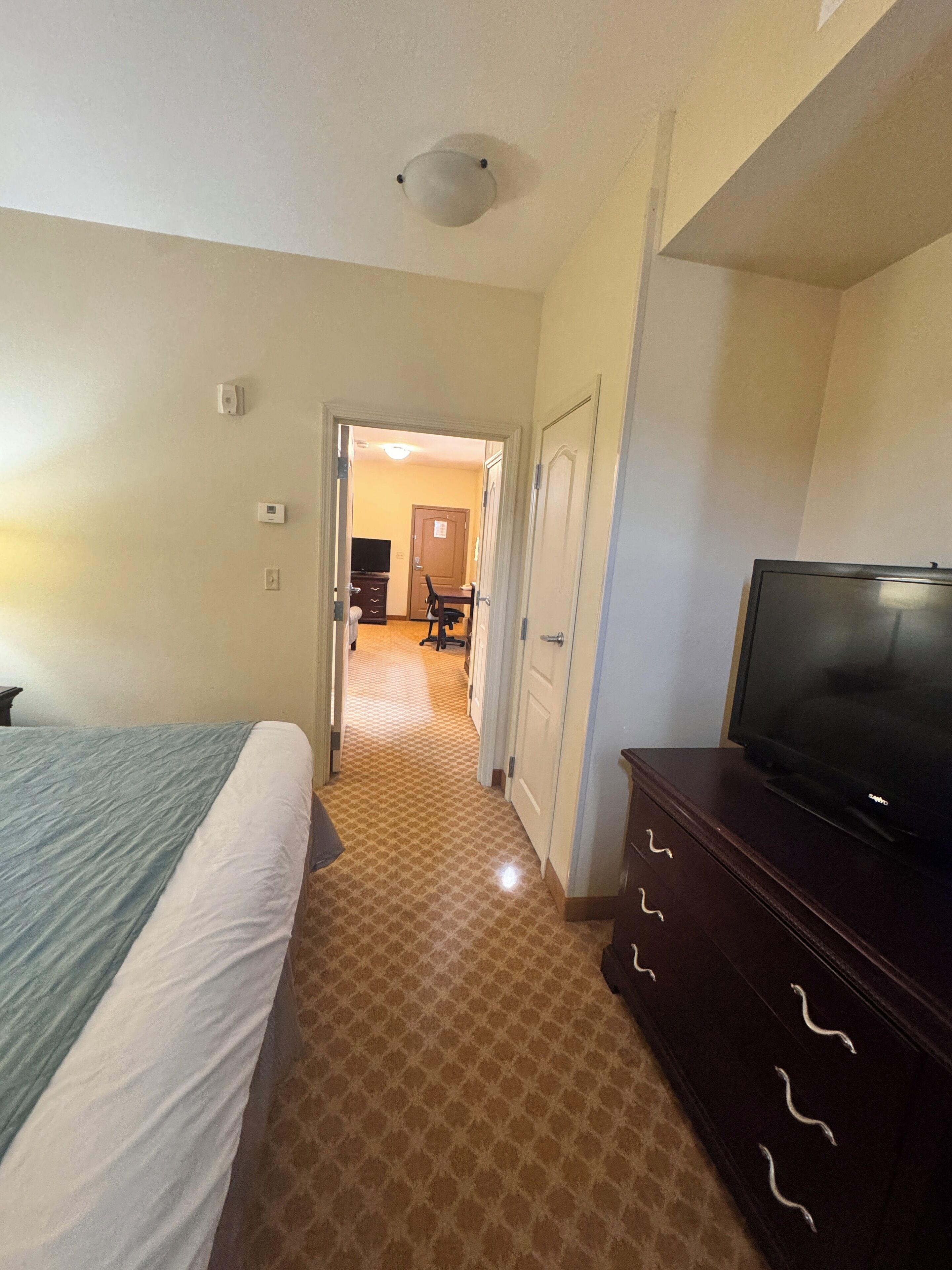 Habitación de hotel con cama, televisor en una cómoda y pasillo que conduce a un comedor.