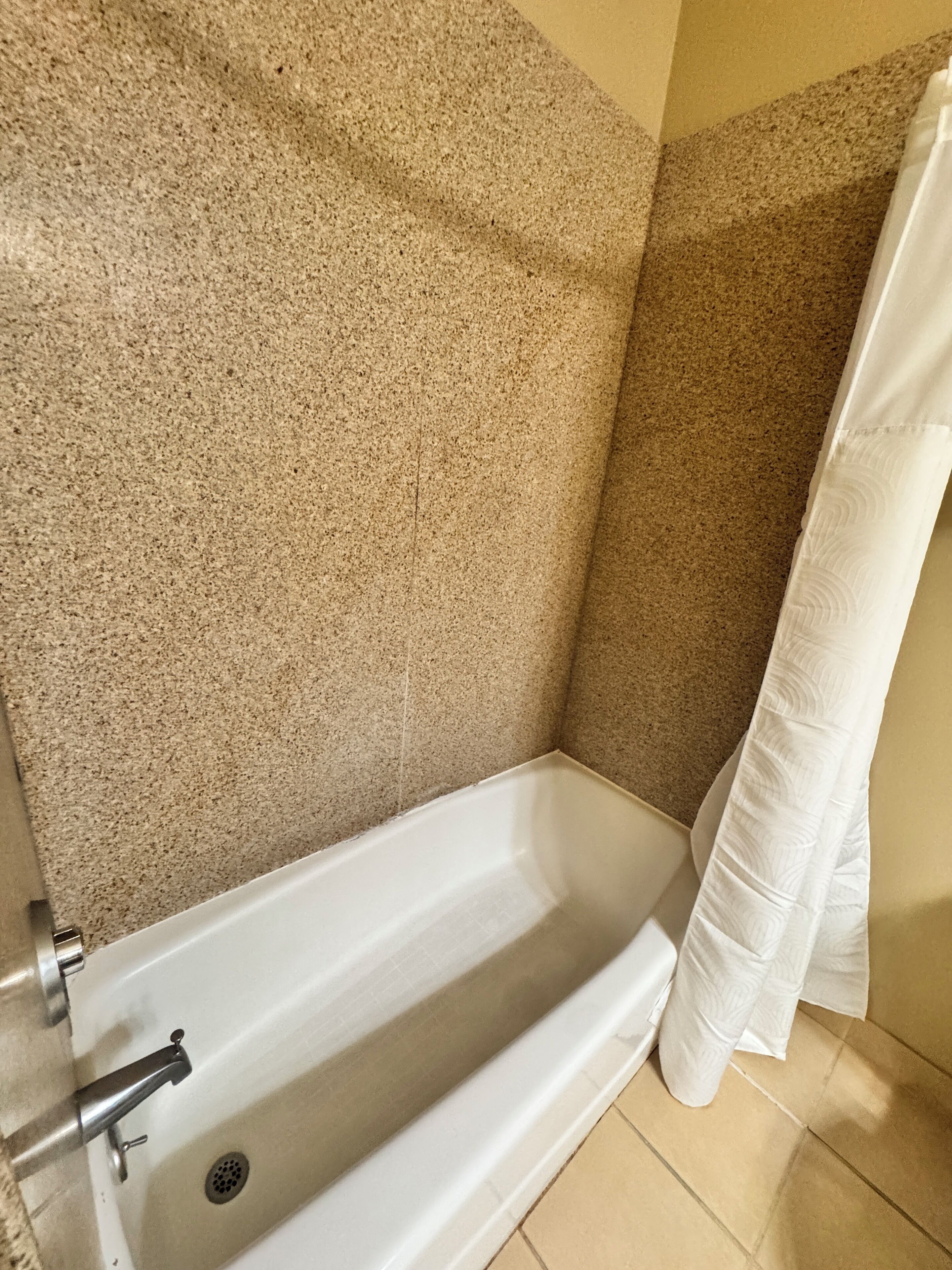 A bathroom with a white bathtub, beige speckled walls, and a white shower curtain.