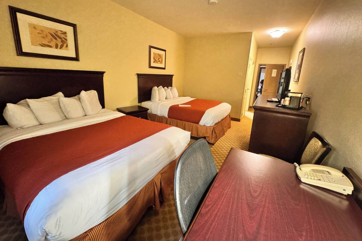 A hotel room with two beds, a desk, a telephone, and a mirror.