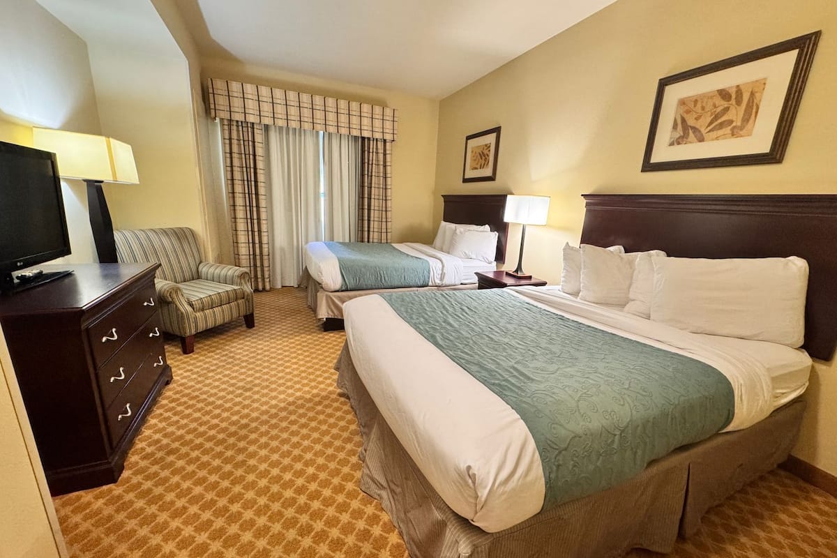 A hotel room with two beds, a television, a dresser, and a chair.