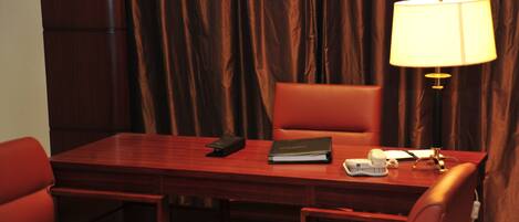 Una habitación de hotel con un escritorio de madera, una silla, una lámpara y un teléfono.