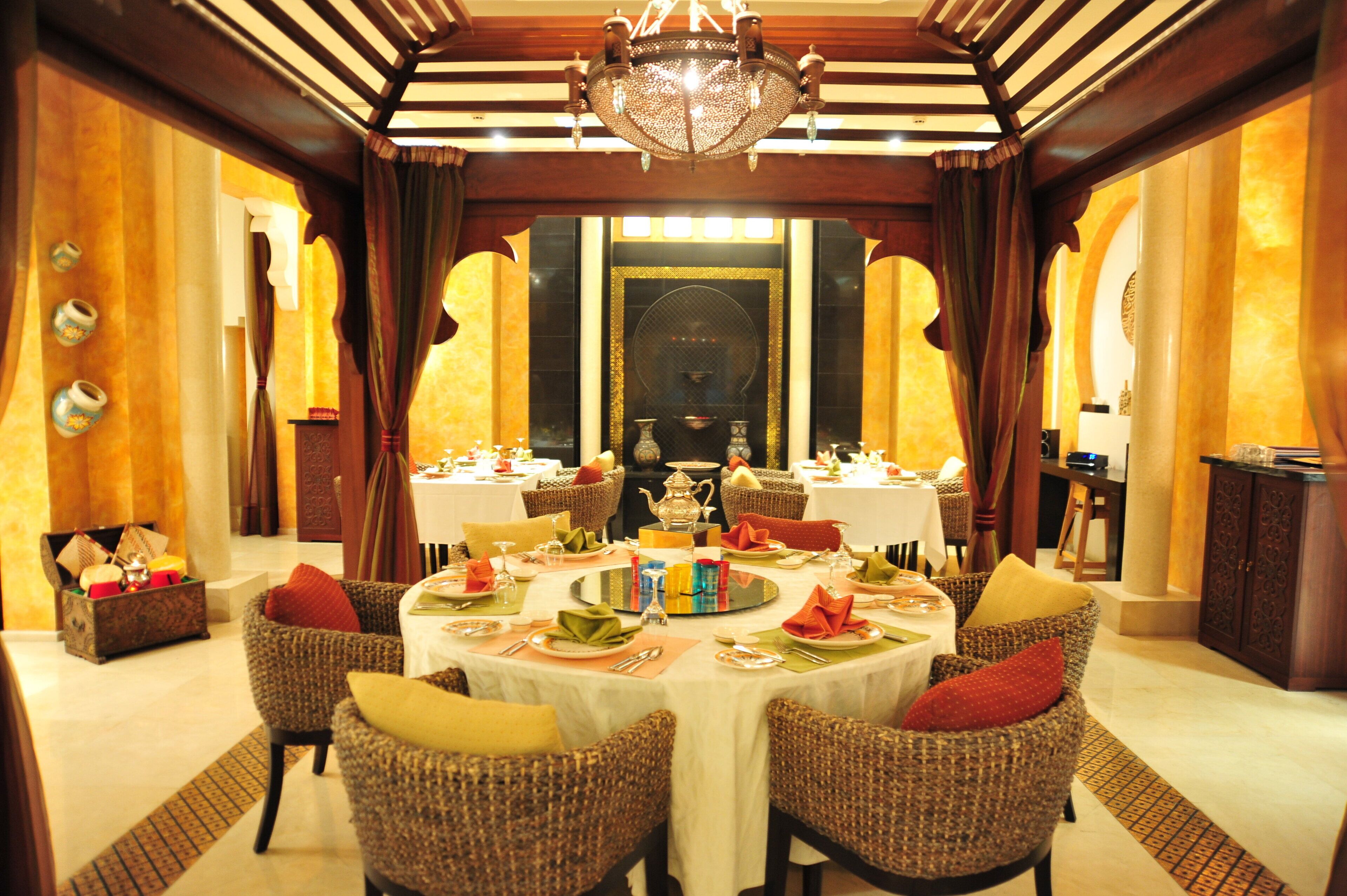 A formal dining room with round tables, wicker chairs, and a chandelier.