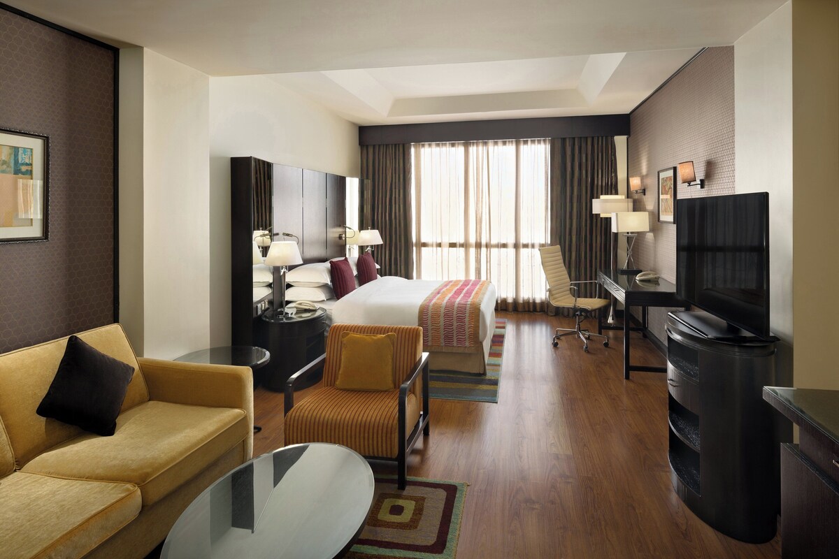 A hotel room with a bed, a sofa, a desk, a television, and a window with curtains.