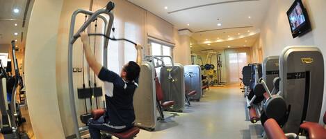 A gym with various exercise machines, a television screen, and a window with blinds.