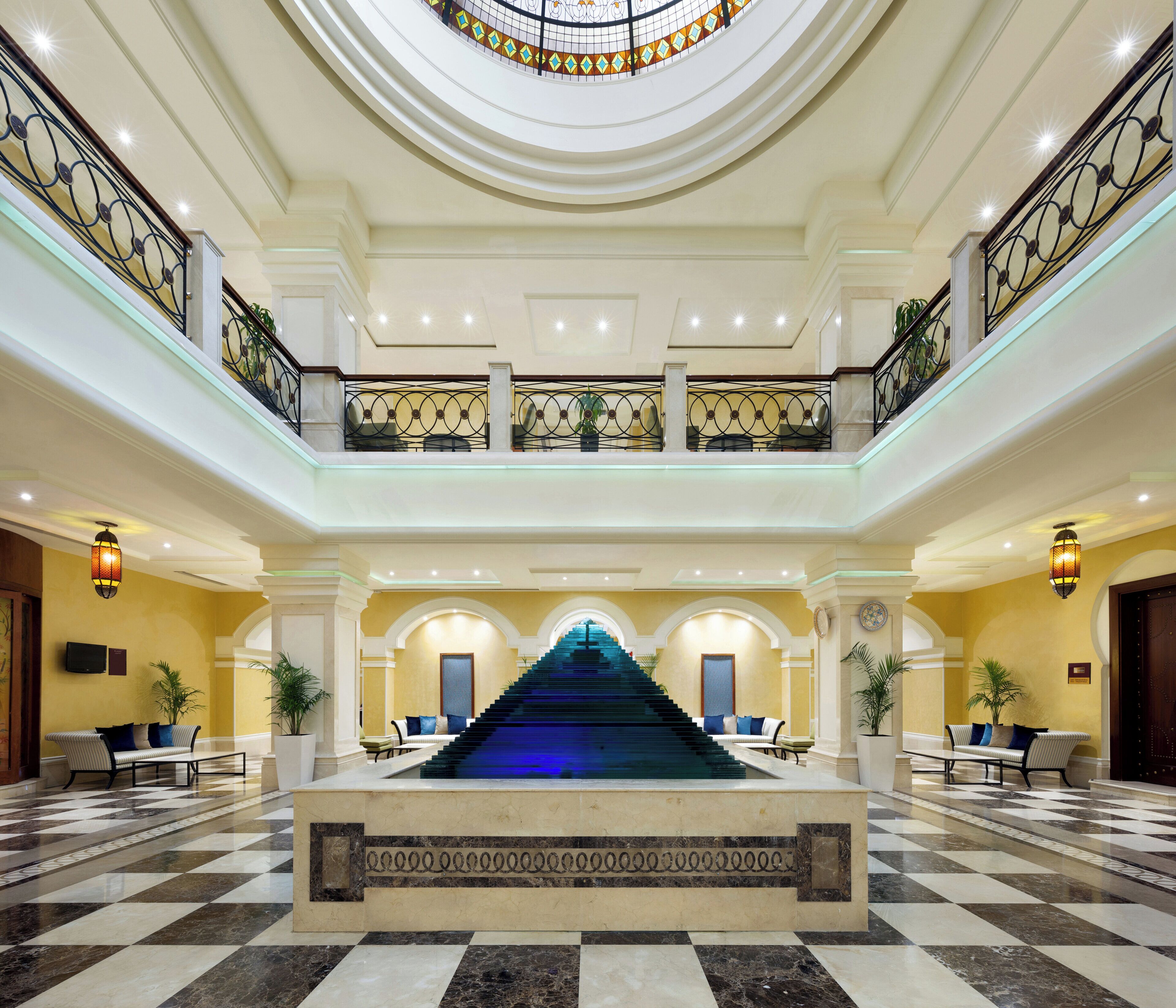 A grand hotel lobby with a central staircase, multiple seating areas, and a decorative ceiling.
