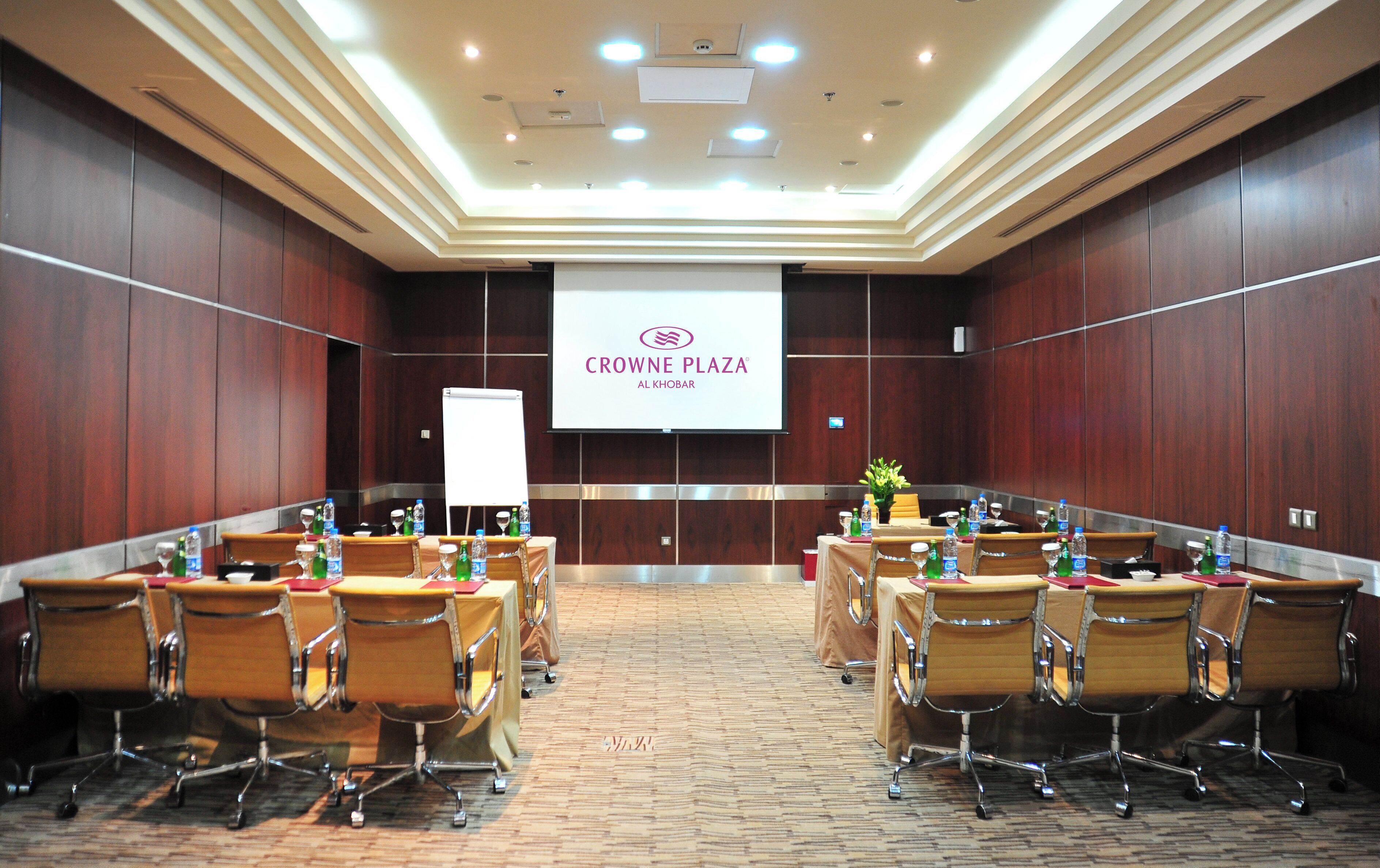 A conference room with a large screen displaying 'CROWNE PLAZA AL KHOBAR' at the front.