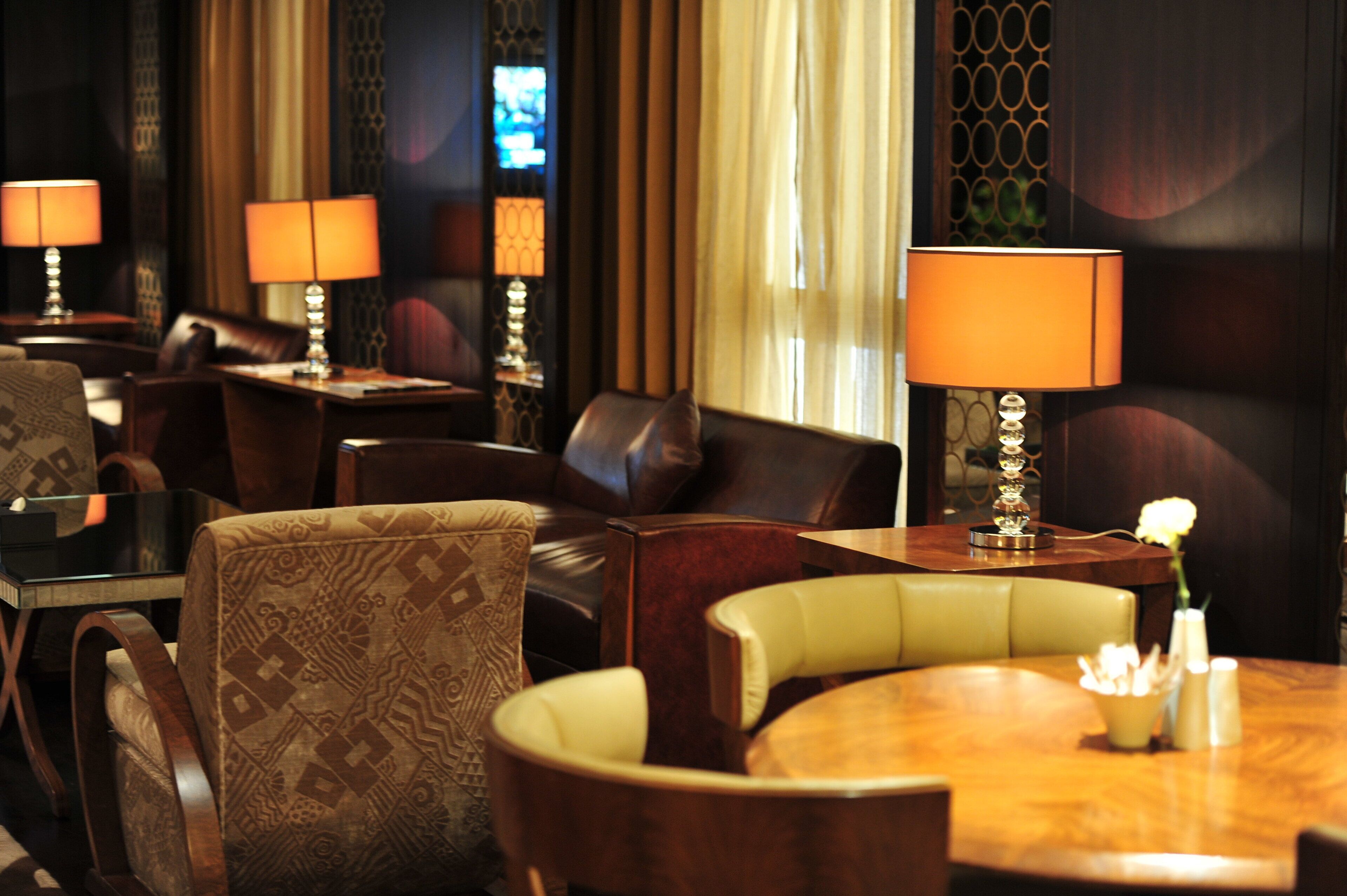A hotel room with a dining area featuring multiple tables with lamps, leather chairs, and a decorative vase with flowers.