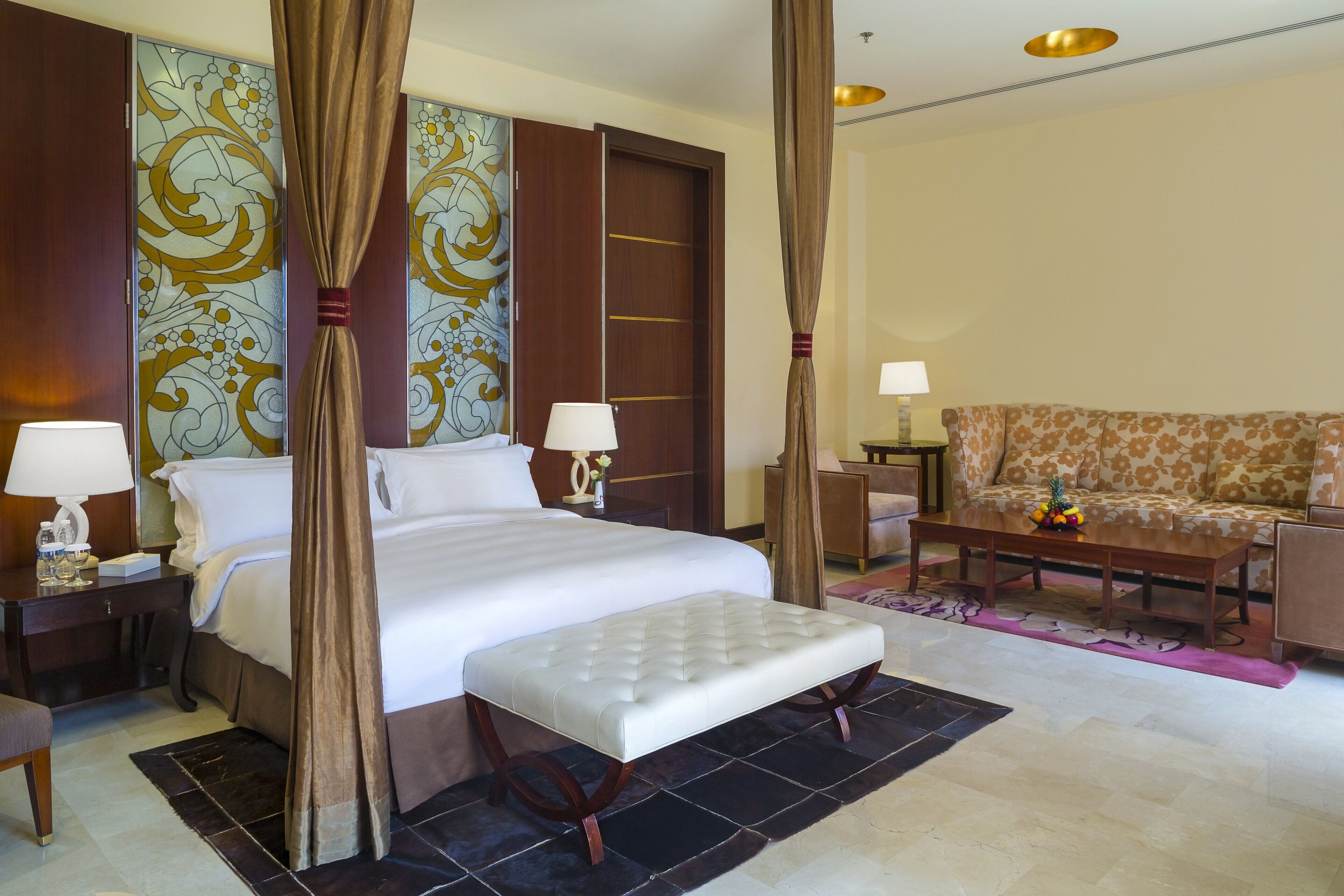 A hotel room with a large bed, a sofa, a desk with a lamp, and a decorative wall.