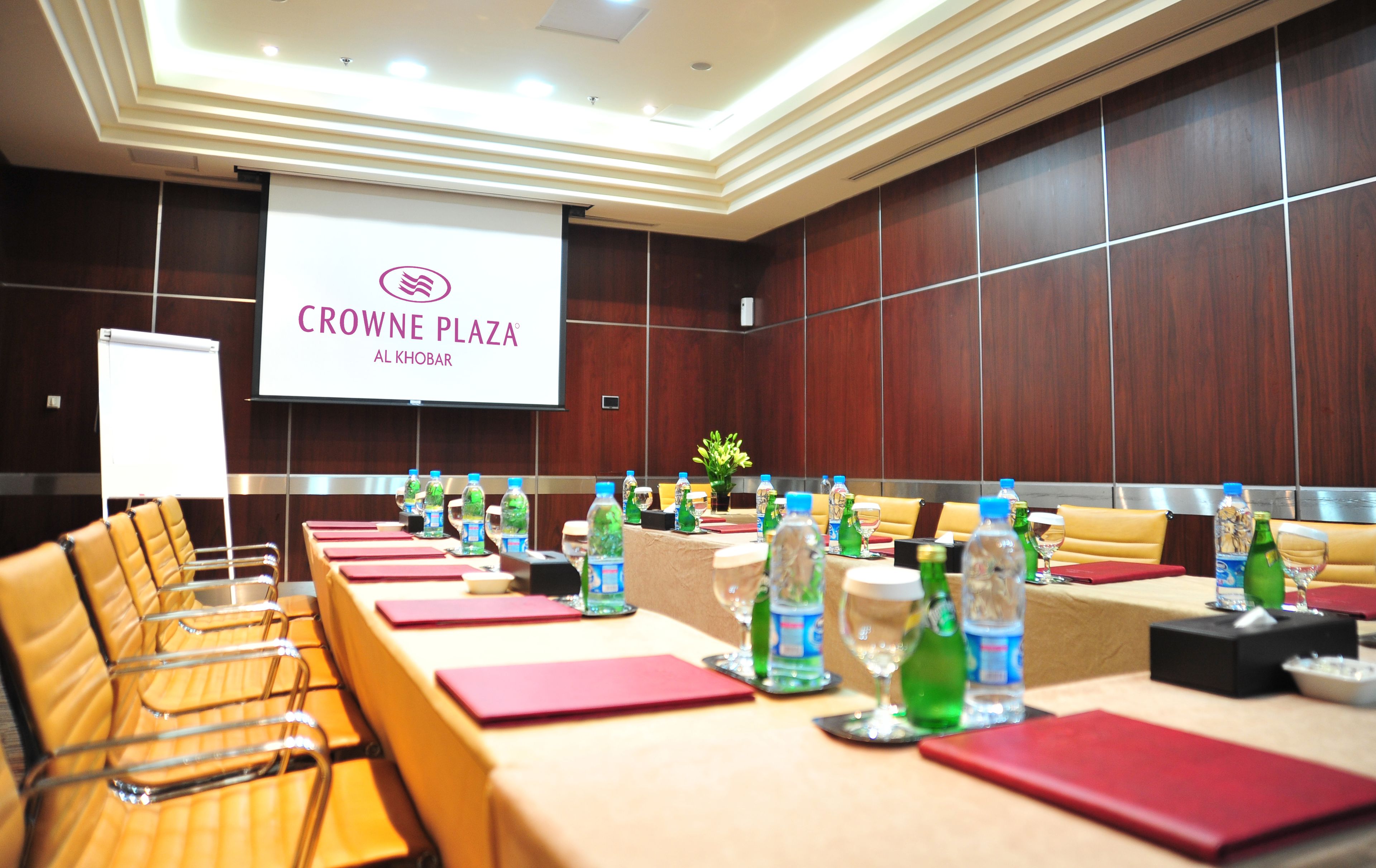 A conference room at Crowne Plaza Al Khobar with a long table set for meetings, equipped with water bottles, glasses, and red folders.