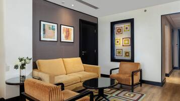 A modern living room with a sofa, two armchairs, a coffee table, and a rug. There are two framed artworks on the wall and a door with a handle.
