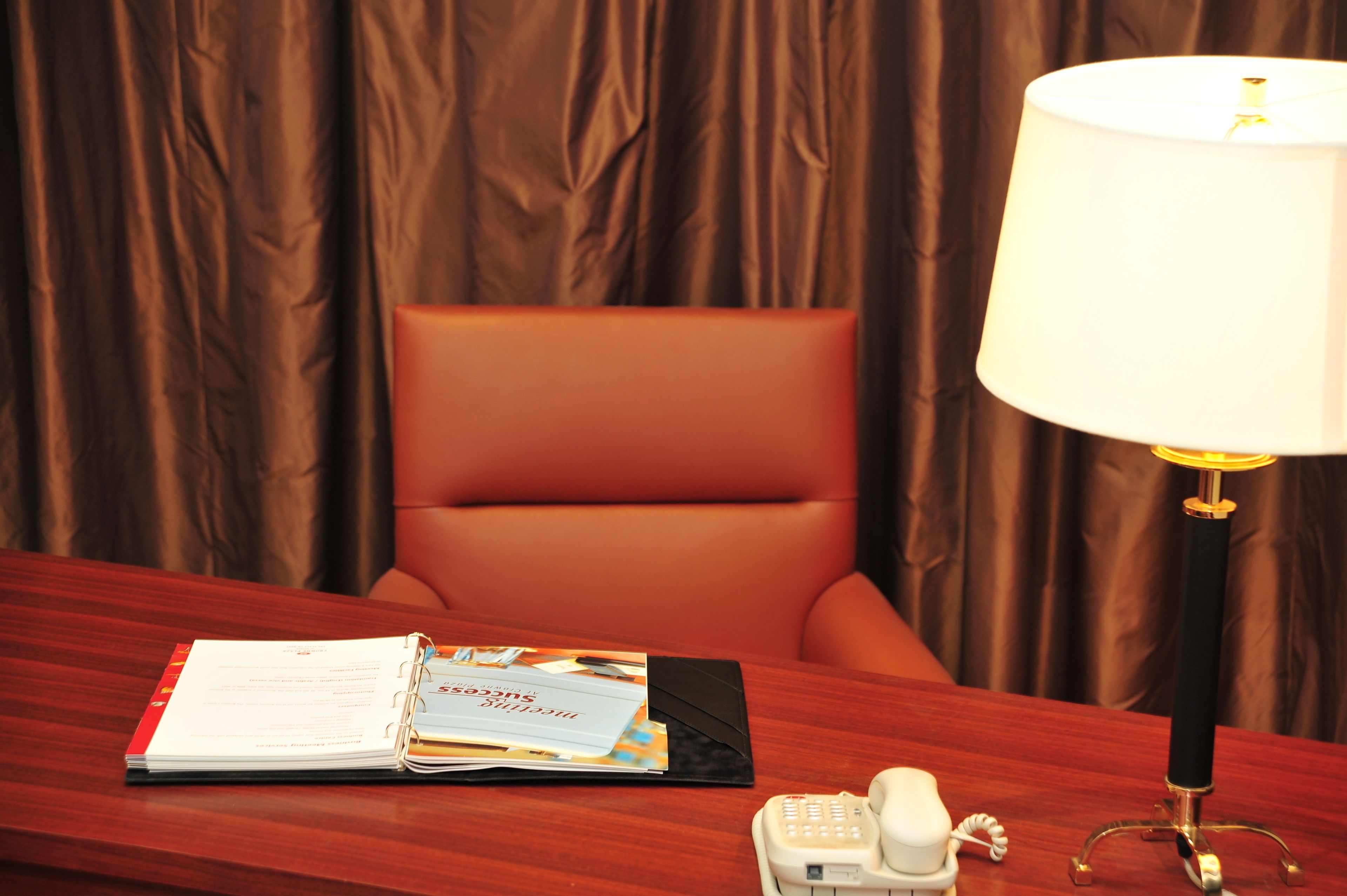 Un bureau en bois avec un téléphone, une lampe et un classeur contenant des documents.