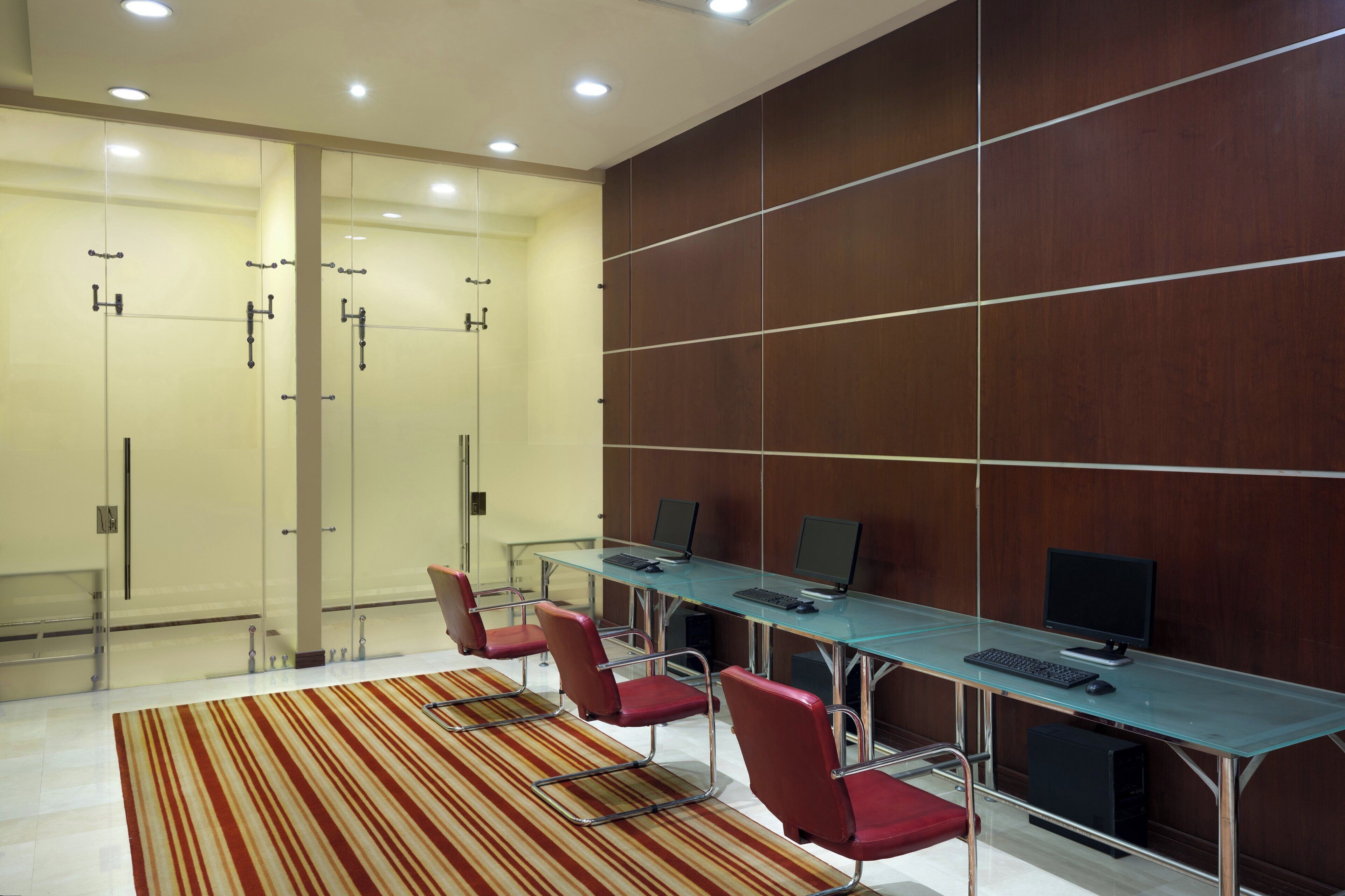 A conference room with glass partitions, a long table with computers, and red chairs.