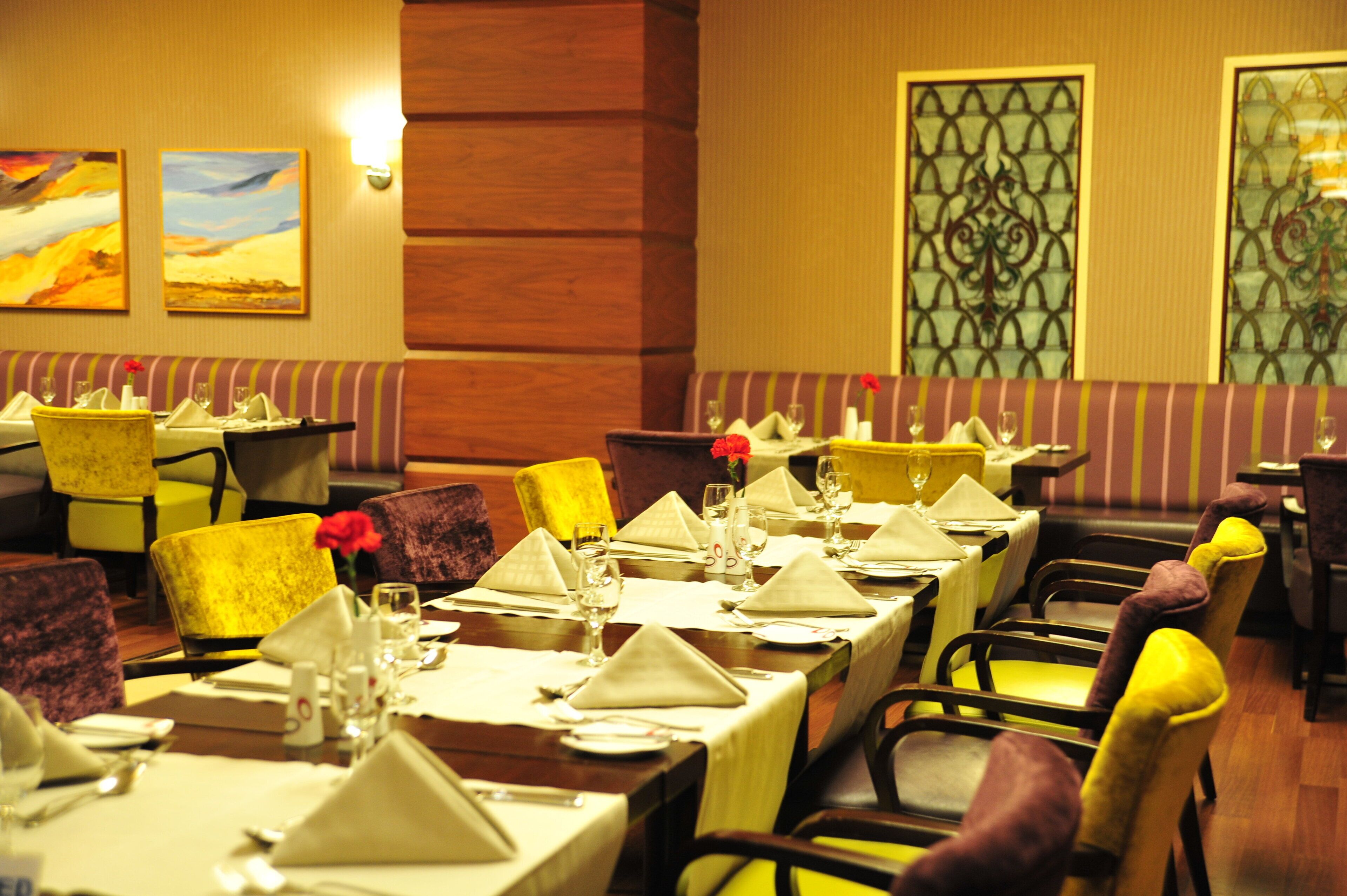 A restaurant with tables set for dining, featuring a variety of chair colors and a decorative wall with a geometric pattern.
