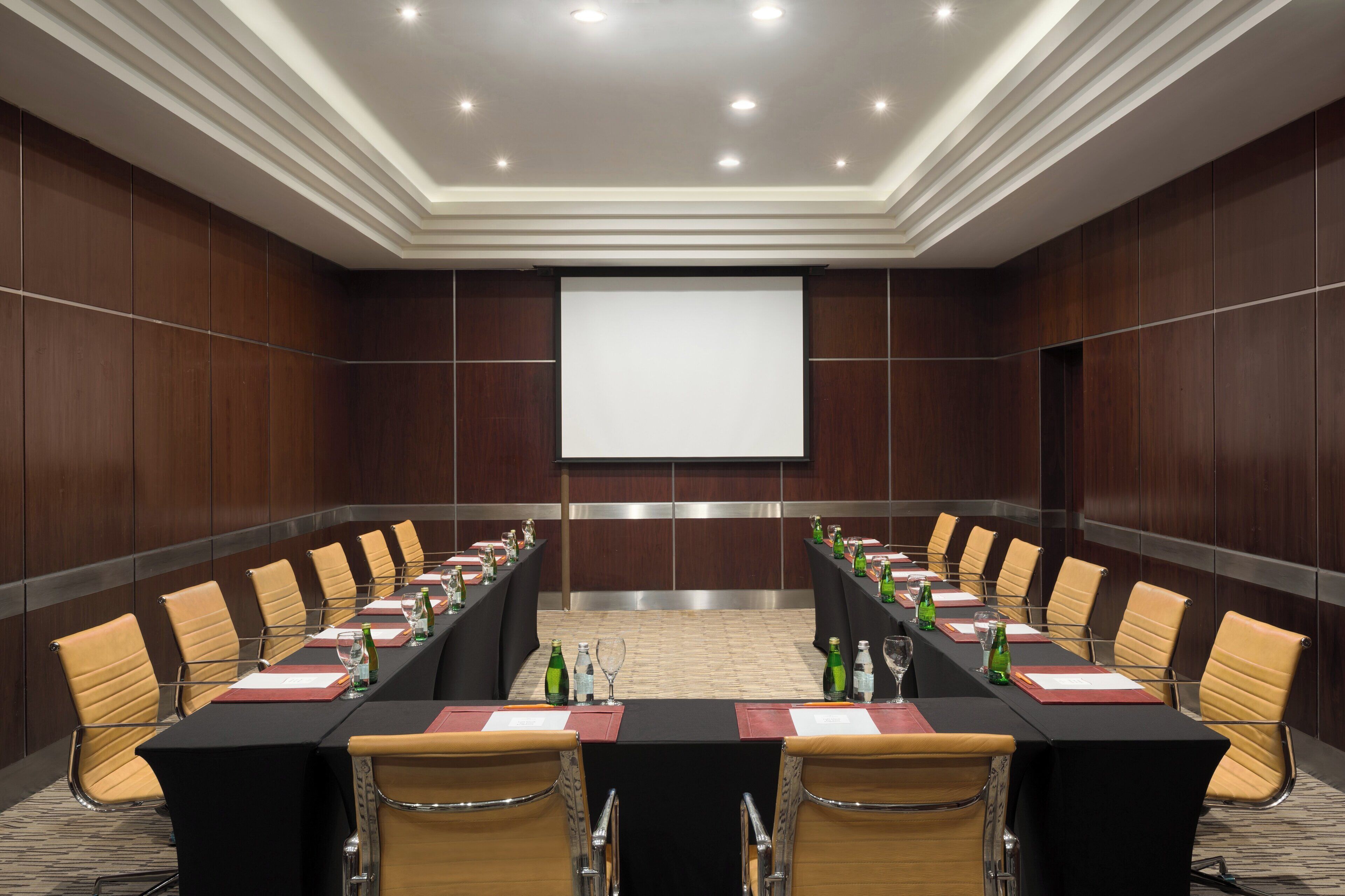 A conference room with a long table, chairs, and a projector screen.