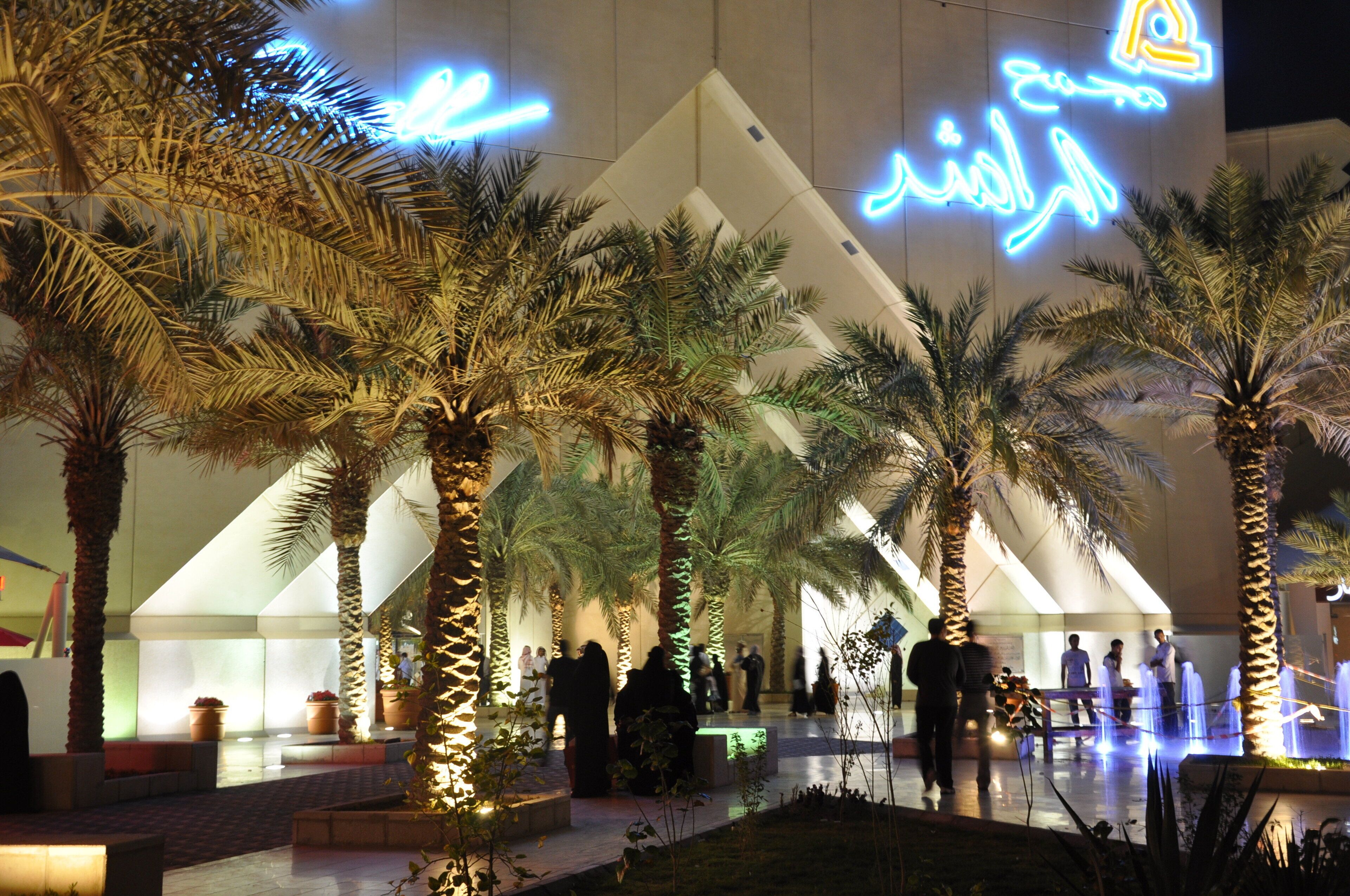 A modern building with illuminated signage, palm trees, and a water feature.