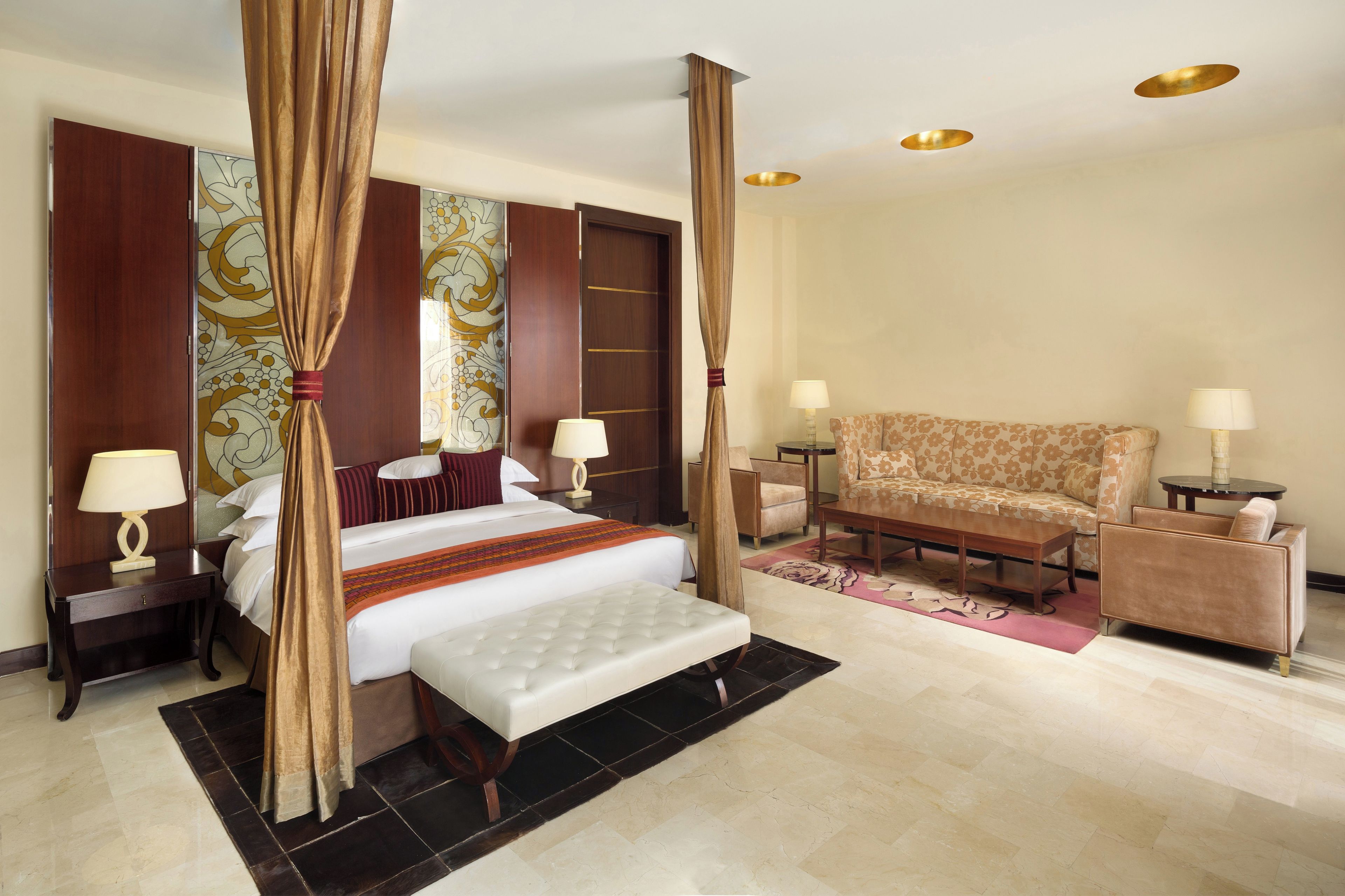 A hotel room with a four-poster bed, a sofa, two bedside tables with lamps, and a large mirror.