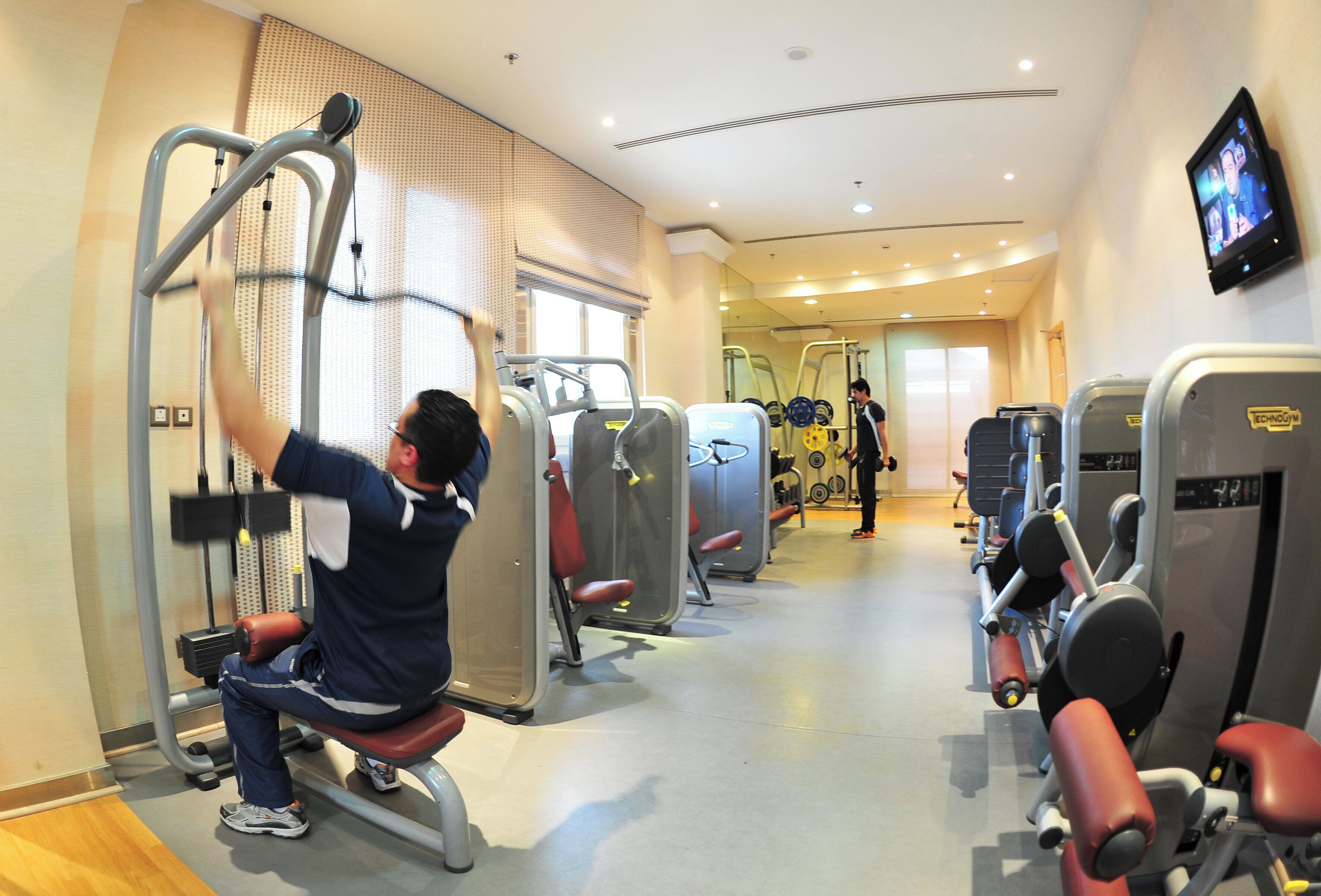 Ein Fitnessstudio mit verschiedenen Trainingsgeräten, einem Fernsehbildschirm und einer Person, die eine Beinpresse benutzt.