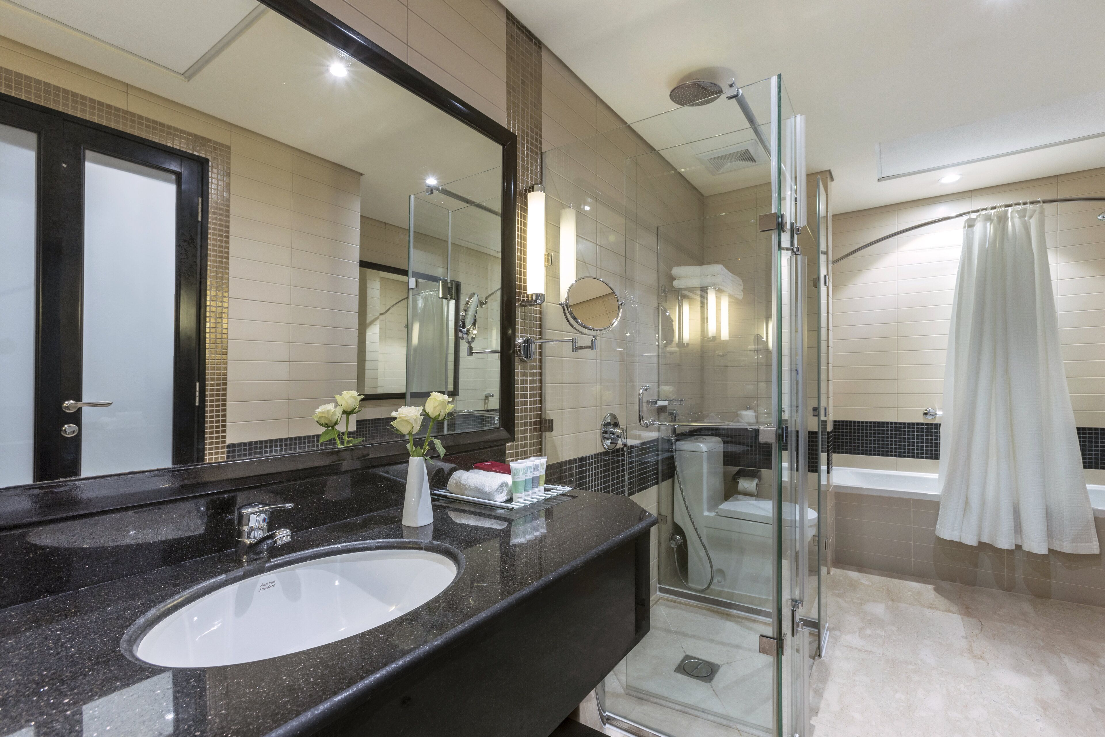 Ein modernes Badezimmer mit einem schwarzen Granittisch, einer Duschkabine aus Glas und einer weißen Badewanne.