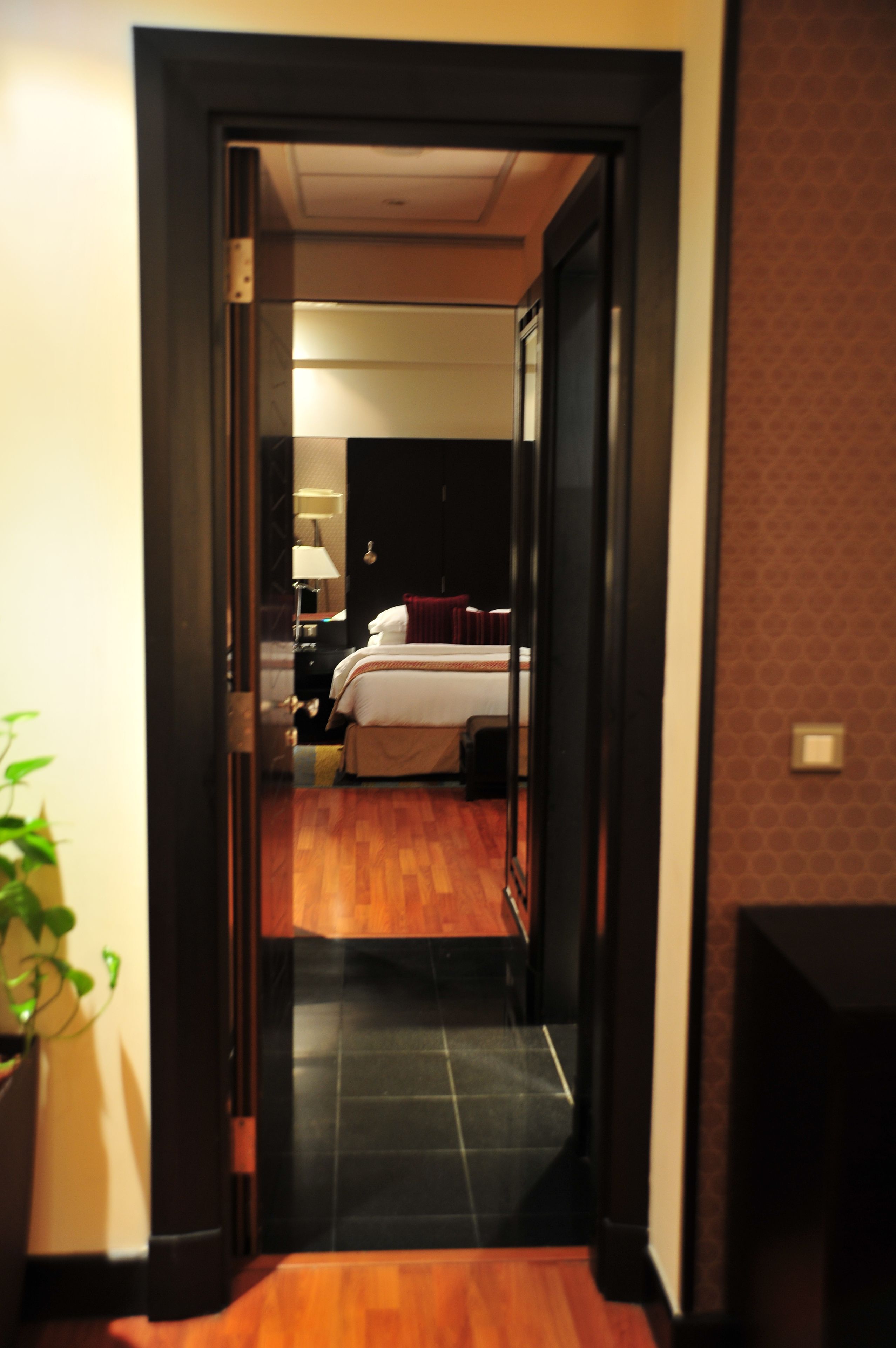 A hotel room with a bed, bedside table, lamp, and a potted plant.