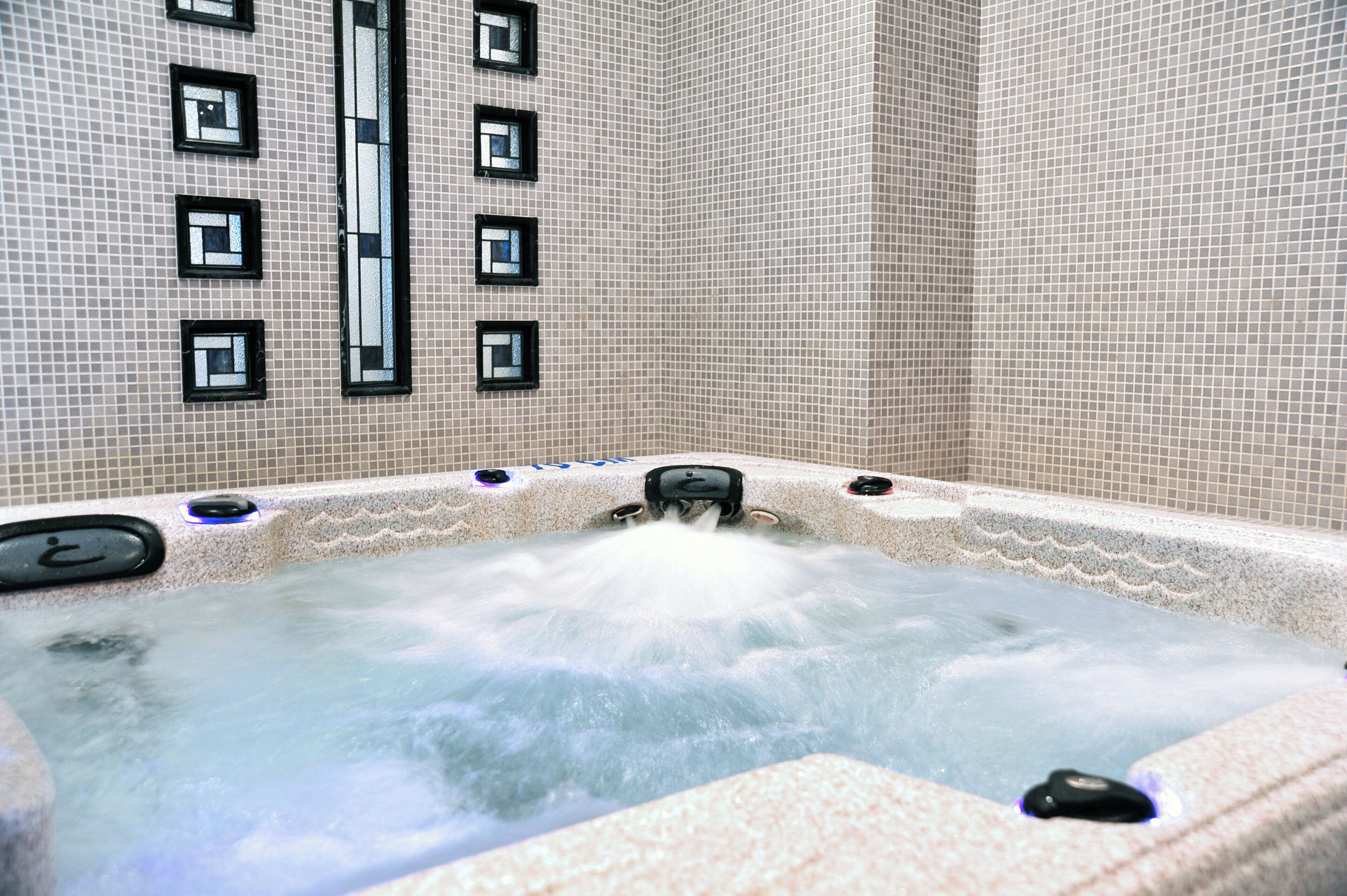 Un jacuzzi con pared de azulejos y varias ventanas.