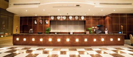 A hotel reception area with a checkered floor, a reception desk, and clocks displaying different time zones.