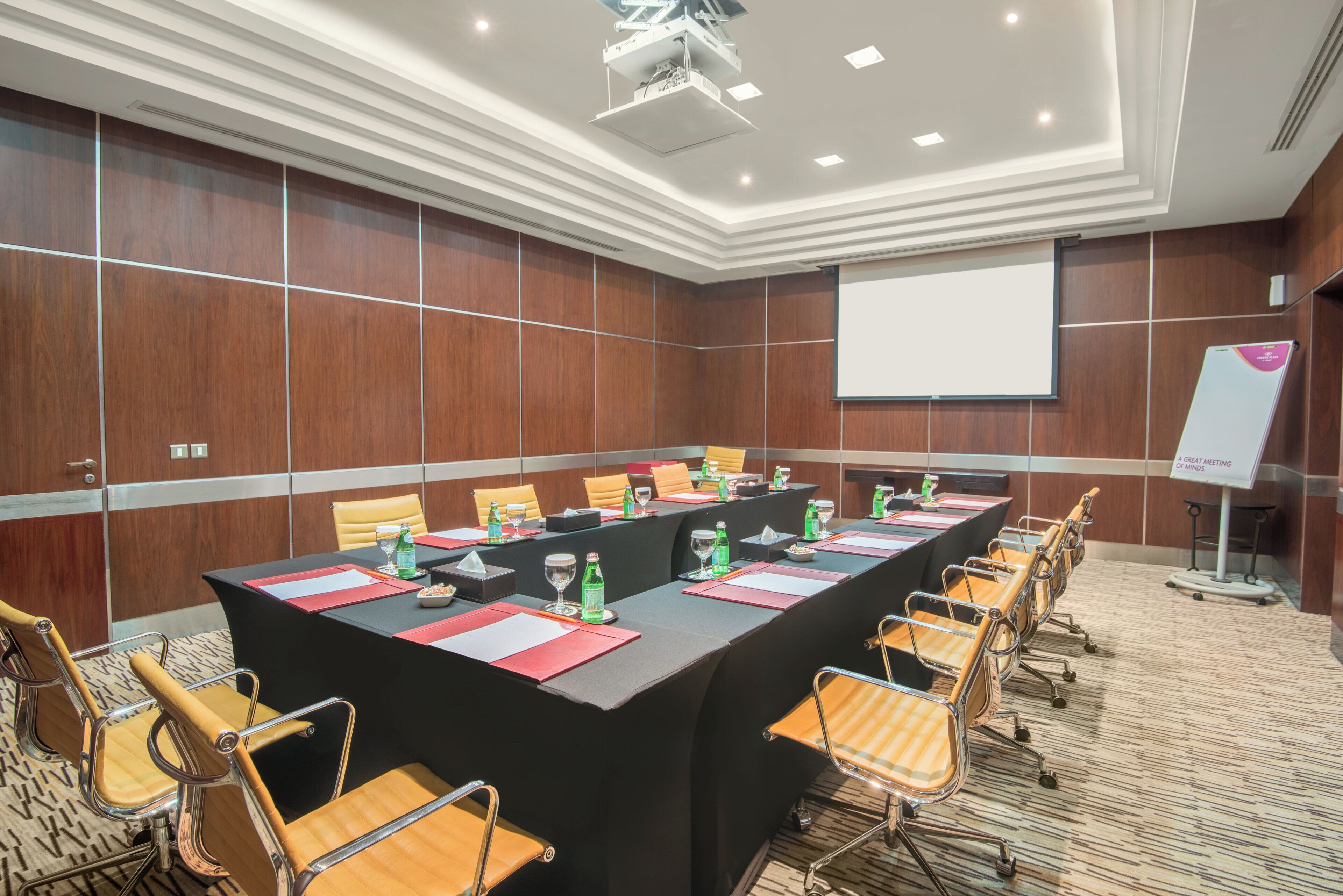 A conference room with a long table, chairs, a projector screen, and a whiteboard.