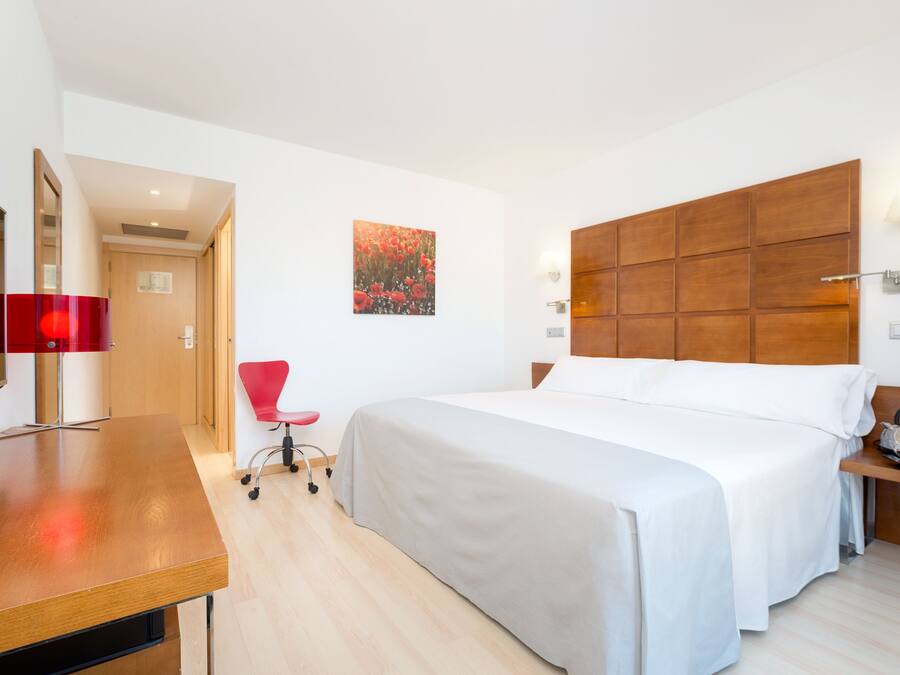 Habitación de hotel con cama, escritorio, silla, cabecero de madera y lámpara fijada a la pared.