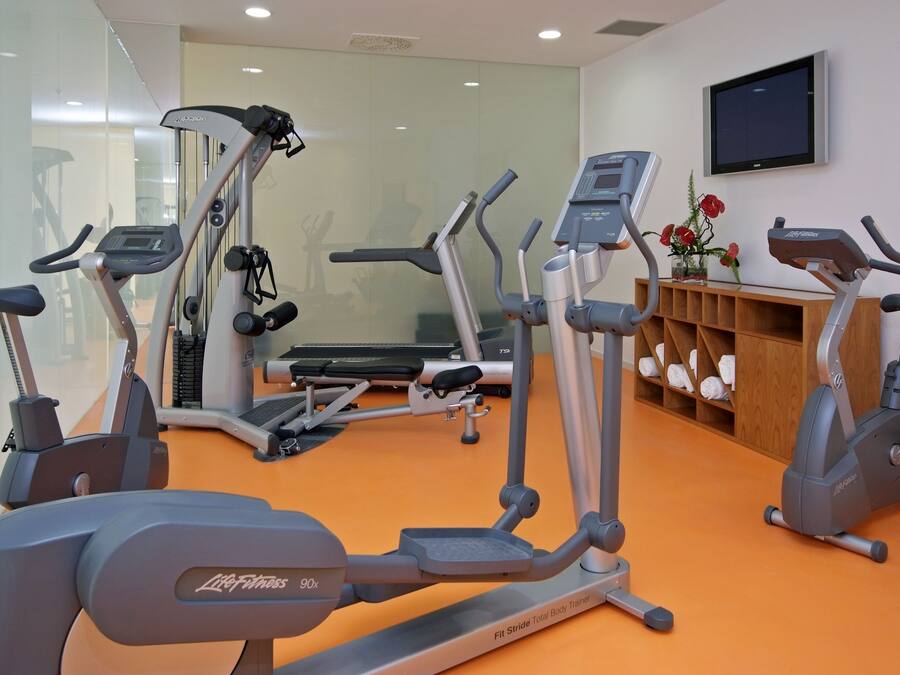 Un gimnasio con cintas de correr, elípticas y un televisor montado en la pared.