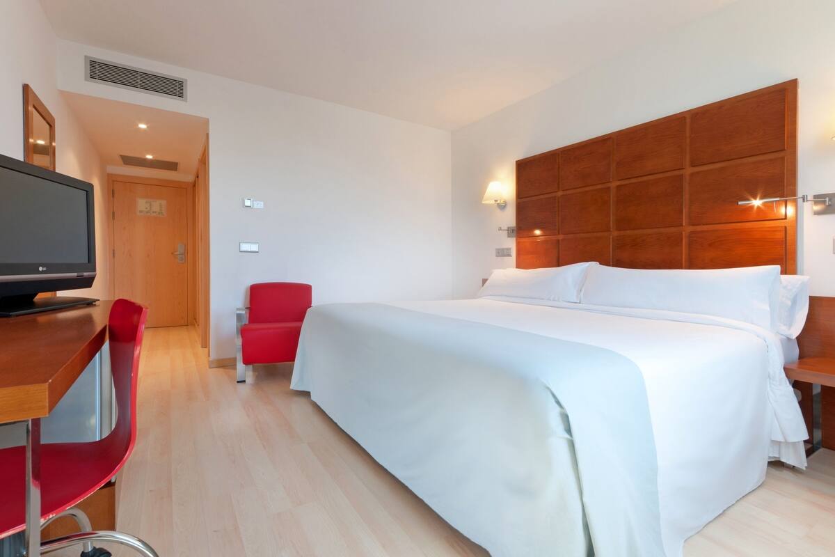 Una habitación de hotel con una cama grande, un televisor, una silla roja y un cabecero de madera.