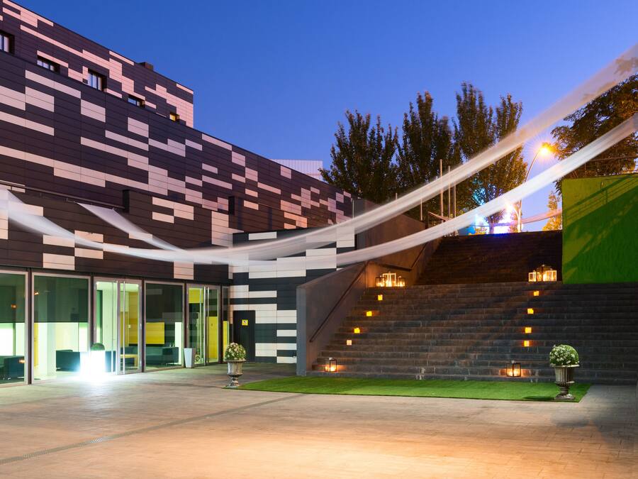 Ein modernes Gebäude mit einer geometrischen Fassade, großen Glasfenstern und einer Treppe, die zu einer oberen Ebene führt.