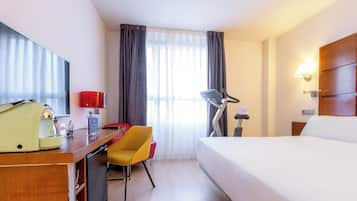 A hotel room with a bed, desk, chair, lamp, and a coffee machine.