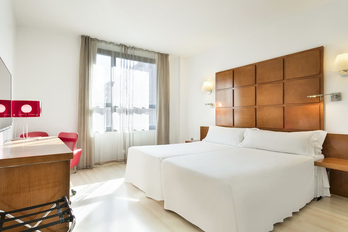 Habitación de hotel con una cama grande, un escritorio con silla y un ventanal con cortinas.