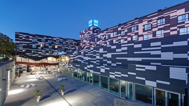 A modern hotel with a unique pixelated facade, outdoor seating area, and a prominent sign. - Zentral Ave (Zaragoza)