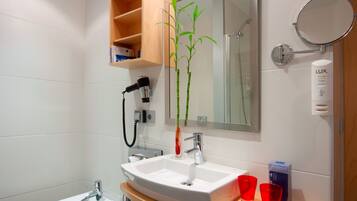 Un baño moderno con un lavamanos blanco, un espejo, una planta de bambú y un estante con artículos de aseo.